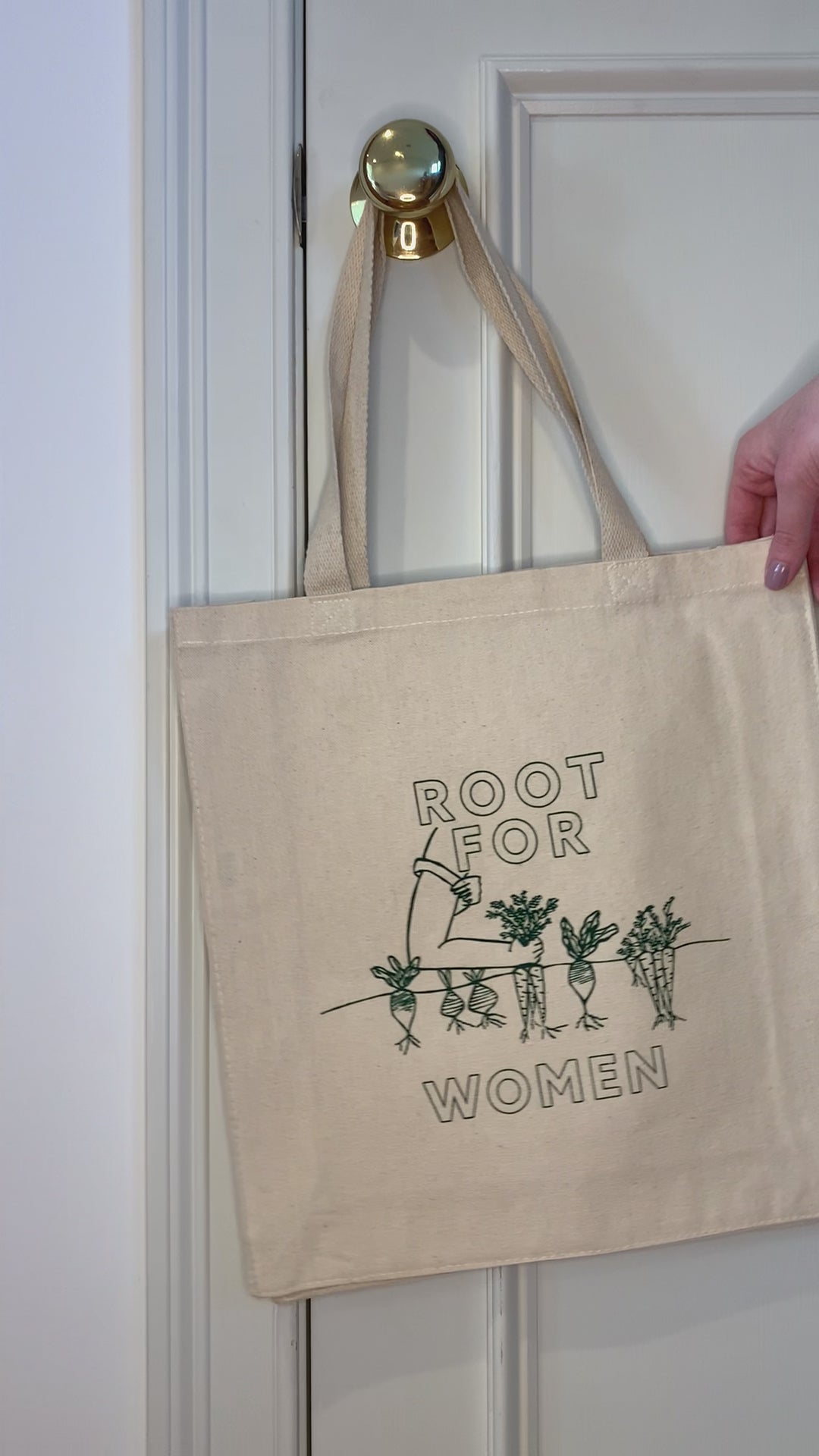 A canvas tote with "Root for Women" in green block letters hangs on a doorknob