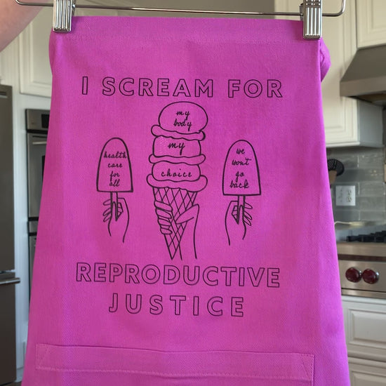 A pink apron that reads "I scream for reproductive justice" hangs on a hanger