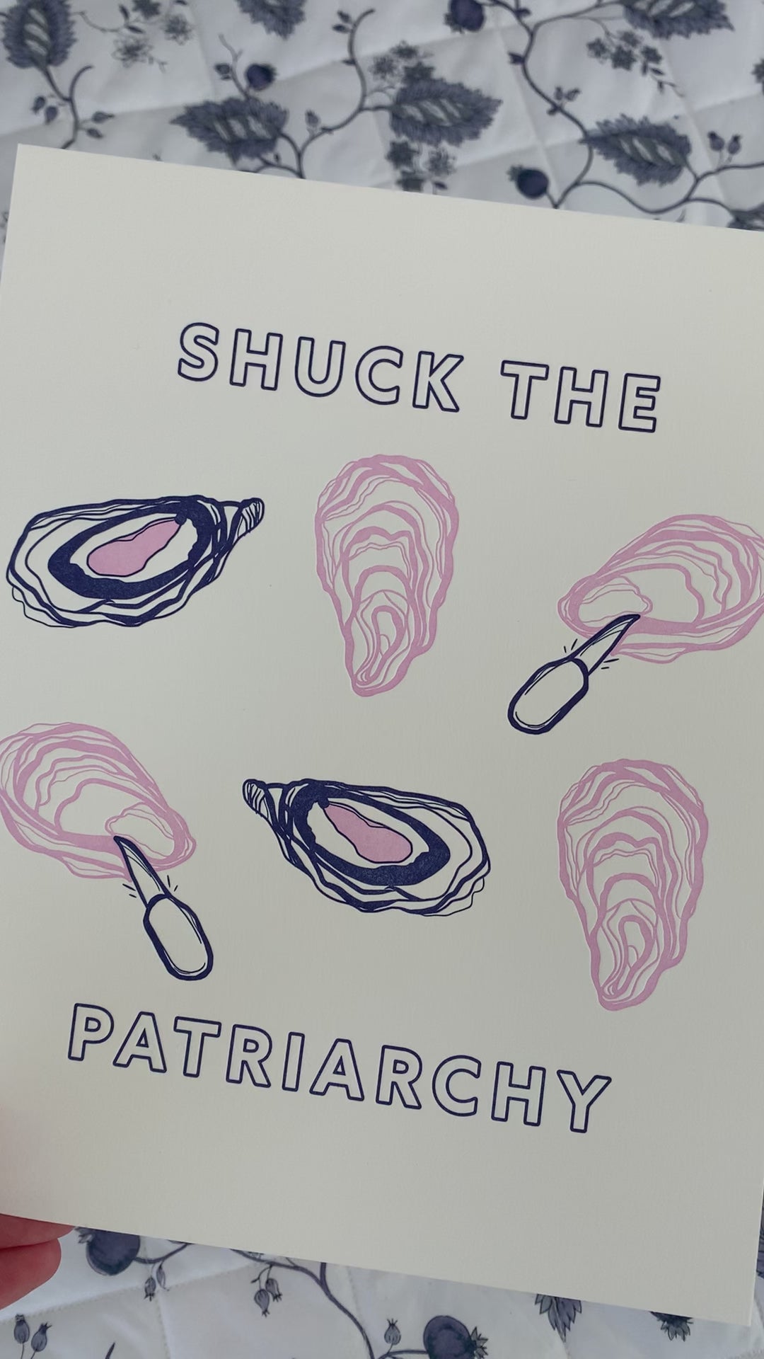 A woman holds an art print that reads "Shuck the Patriarchy" with oyster illustrations 