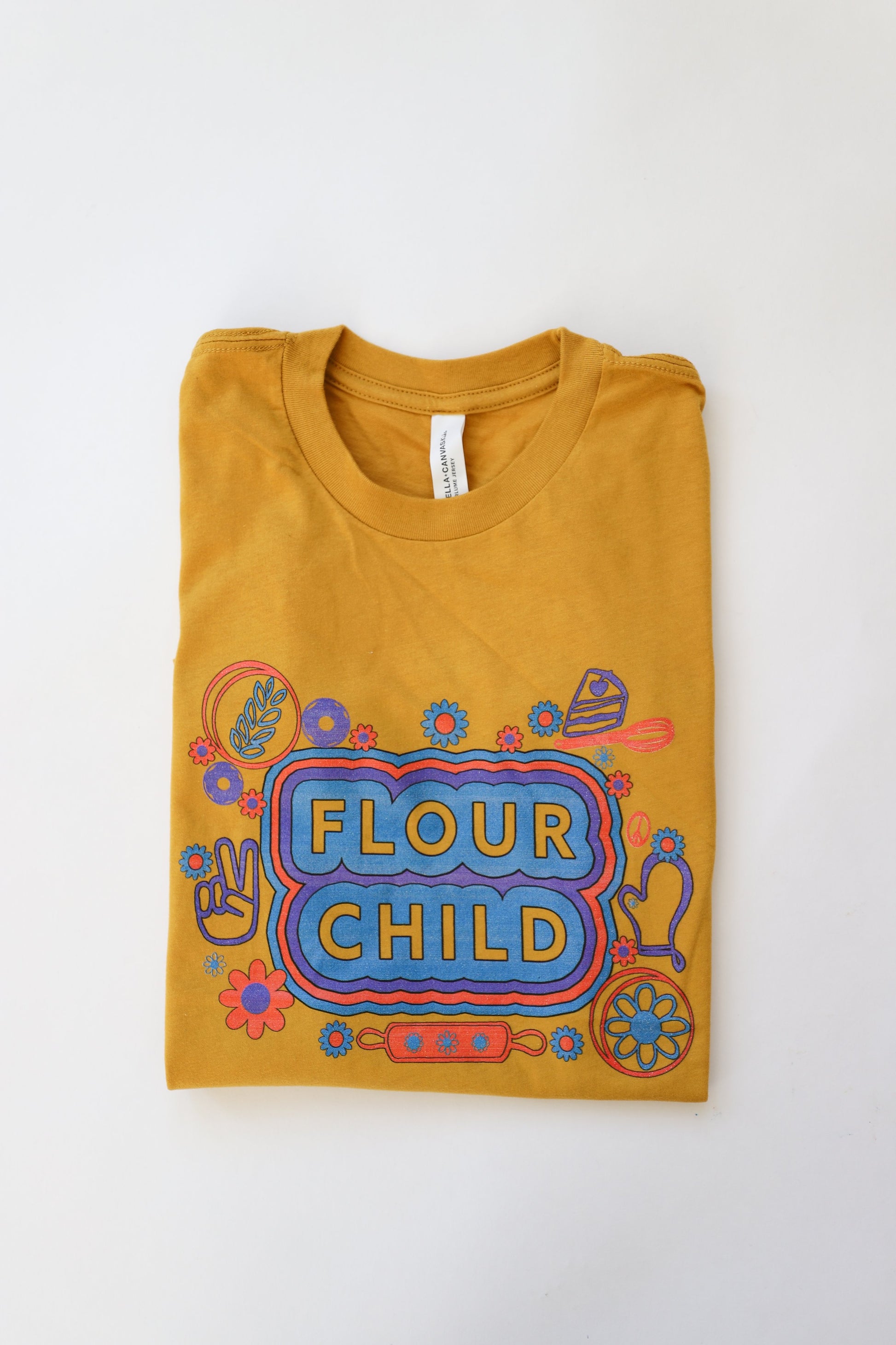 A folded yellow youth tee with the words Flour Child and fun kitchen illustrations 
