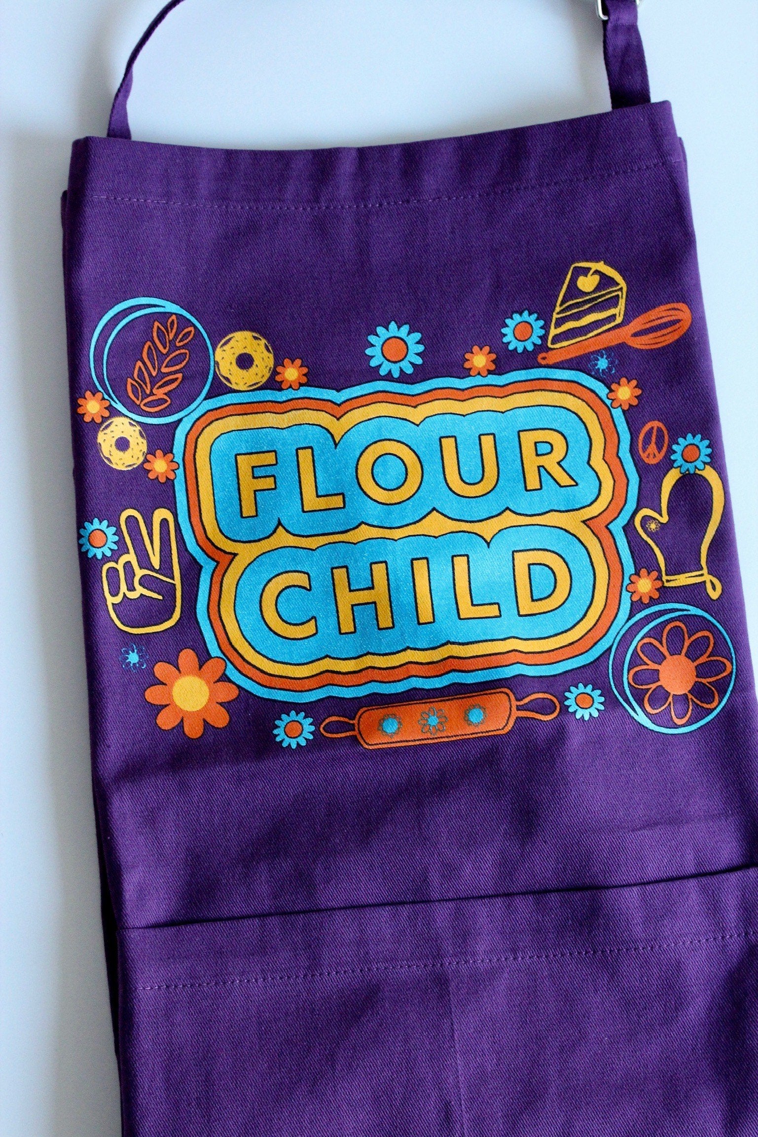 Purple apron with the words Flour Child and kitchen illustrations in yellow, orange and blue