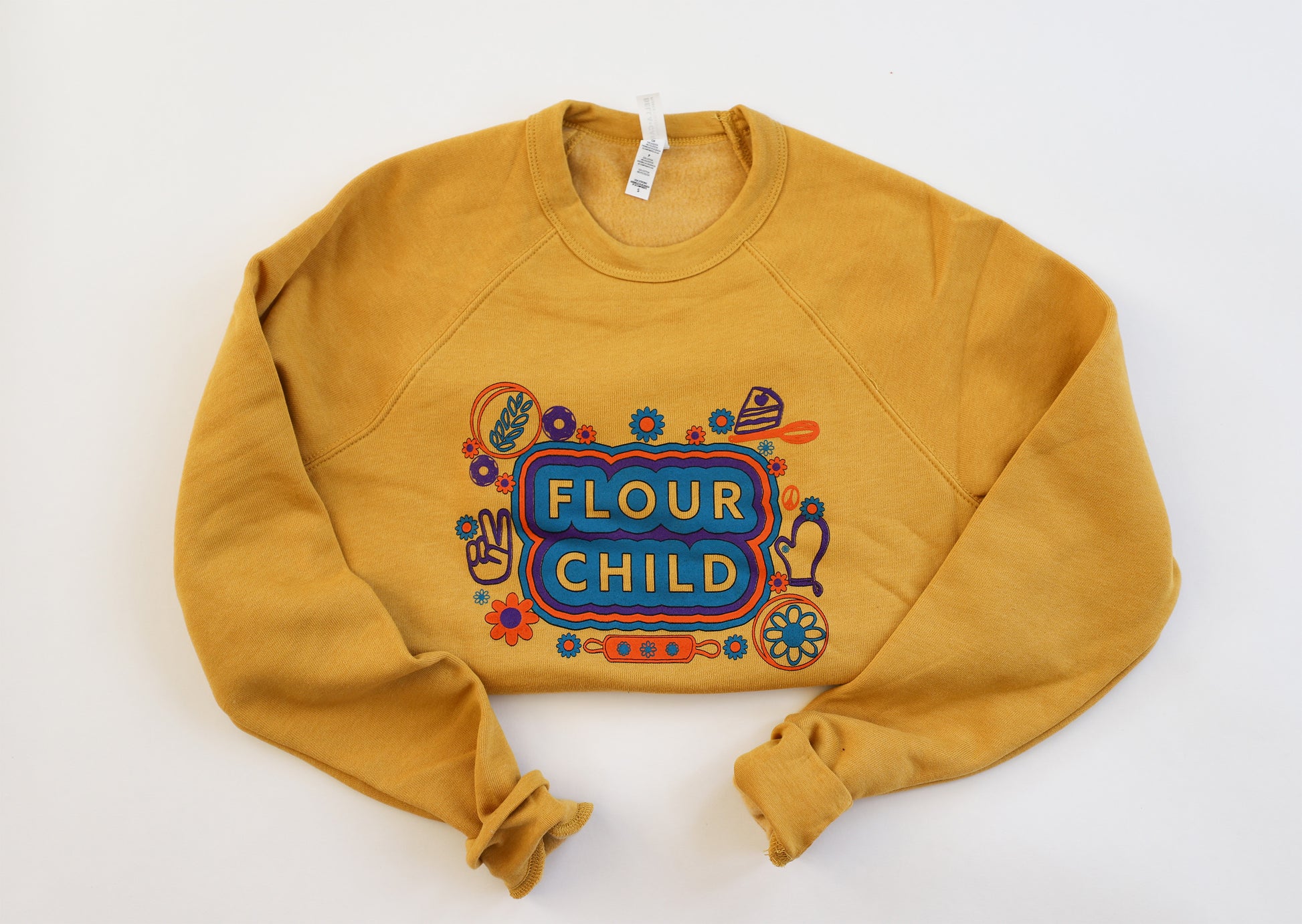 A bright yellow crewneck sweatshirt with the words Flour Child in block letters surrounded by colorful designs.