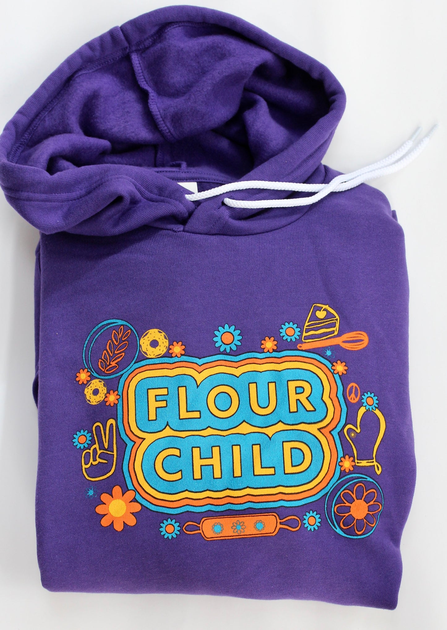A folded purple hoodie with white drawcords and the words "Flour Child" with brightly colored accents and illustrations