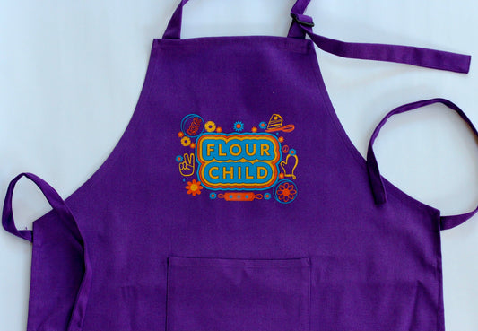 A kid size purple apron with the words Flour Child in block letters with yellow, orange and blue highlights and illustrations