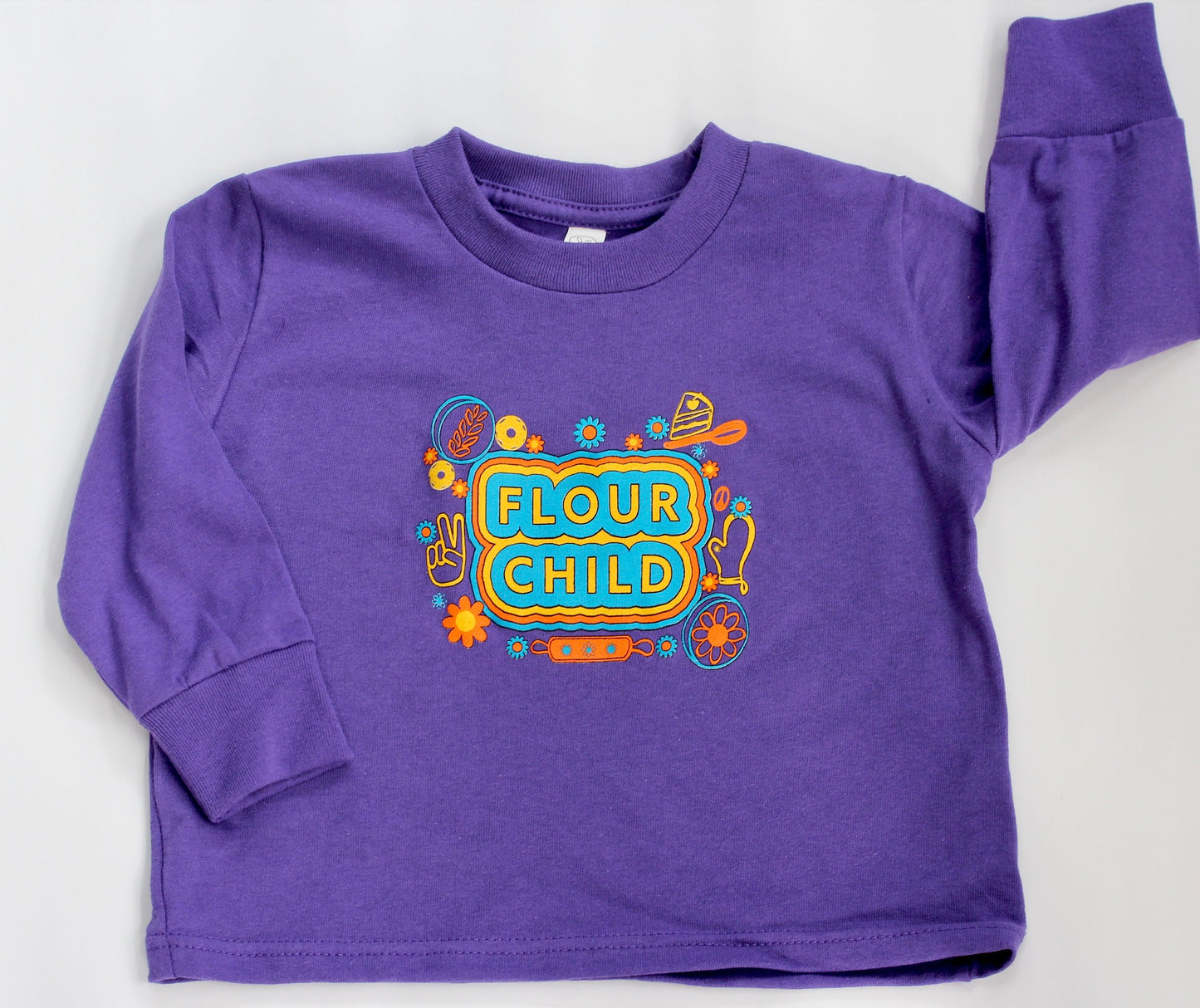 A long sleeve purple toddler tee with the words Flour Child in block letters surrounded by yellow, orange and blue illustrations
