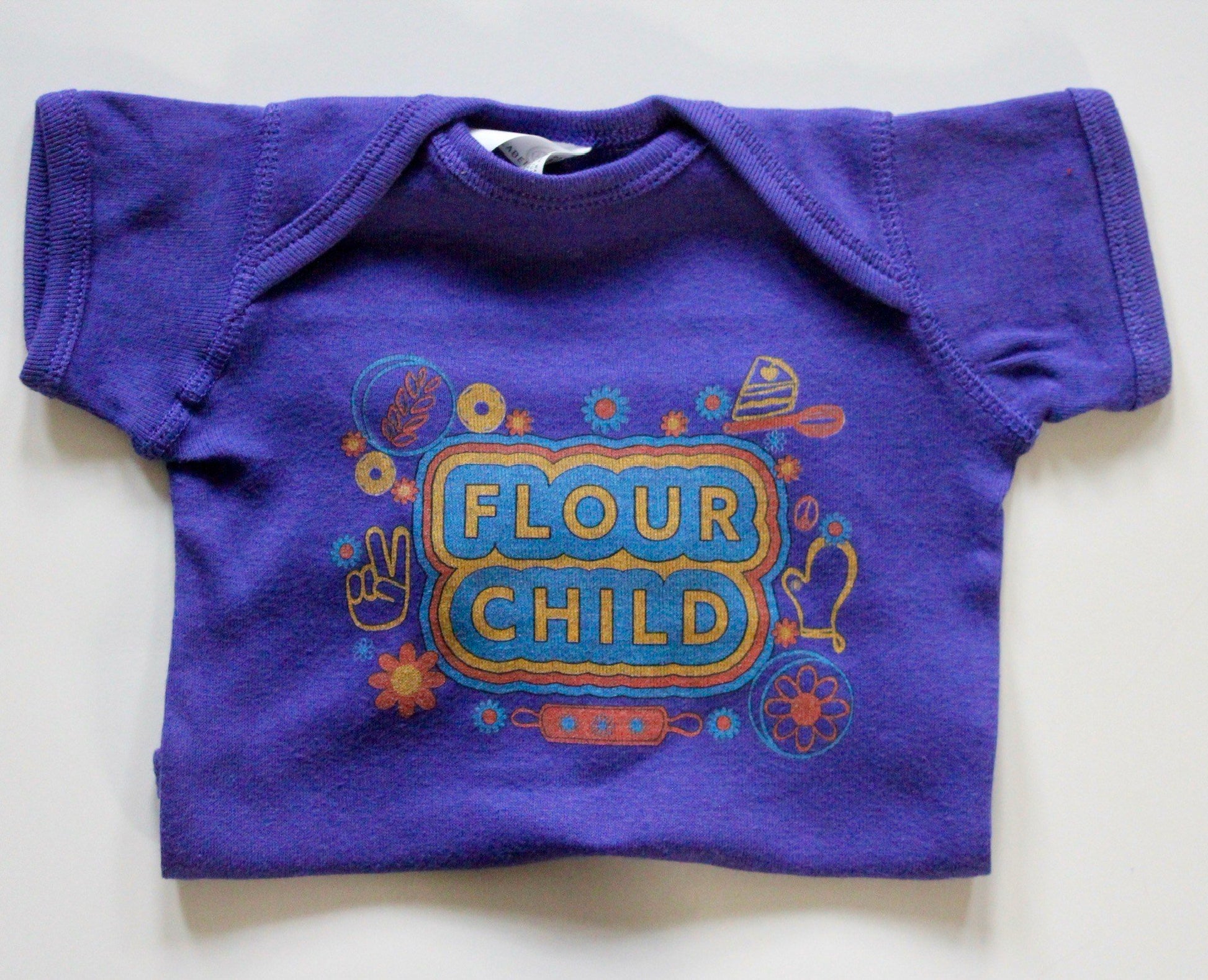 A folded purple baby onesie with the words "Flour Child" and colorful illustrations