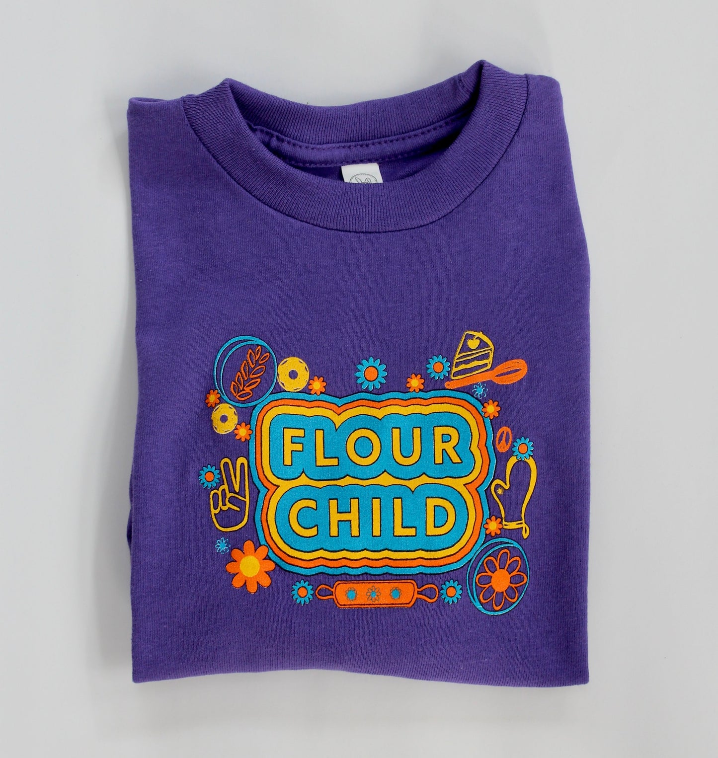 A folded long sleeve purple toddler t-shirt with the words Flour Child and colorful designs
