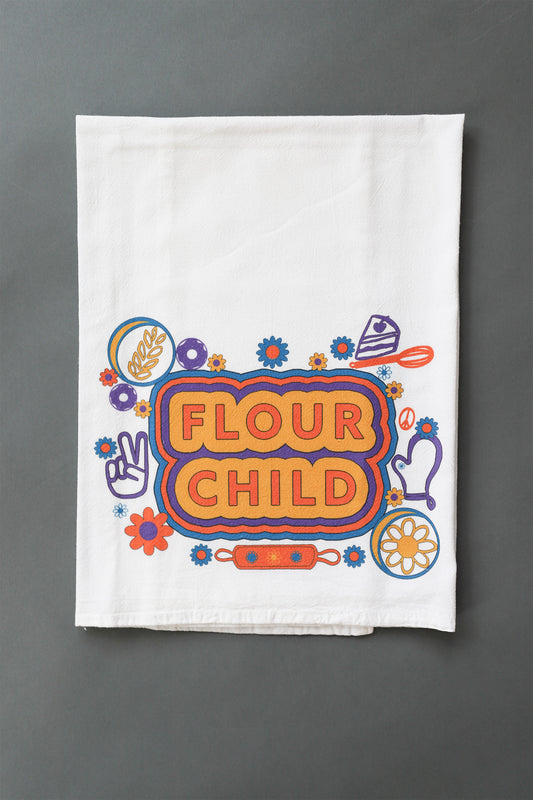 A white tea towel with the words Flour Child and kitchen and hippie illustrations in yellow, orange, blue and purple