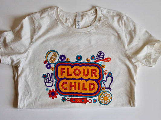 A white women's tee with the words Flour Child in block letters and colorful kitchen illustrations