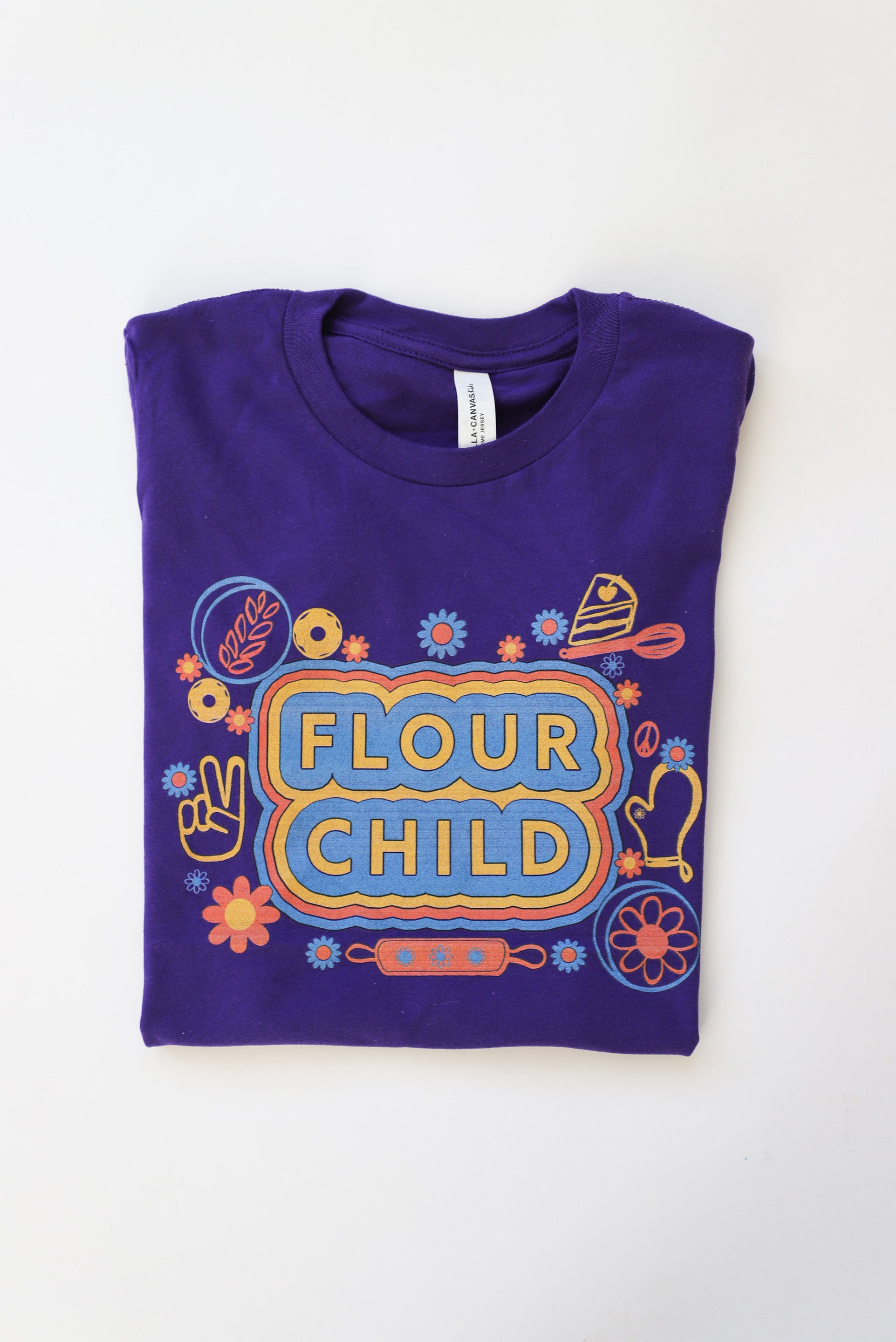 A folded purple youth t-short with "Flour Child" in block letters surrounded by bright illustrations