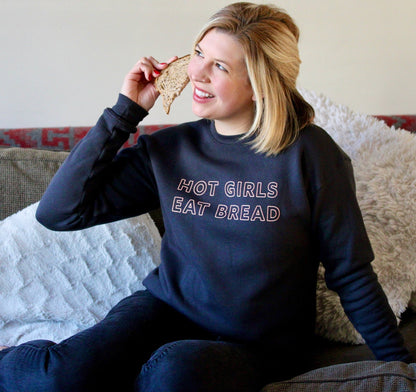 A woman wears a grey sweatshirt that says "Hot Girls Eat Bread" and holds a slice of bread