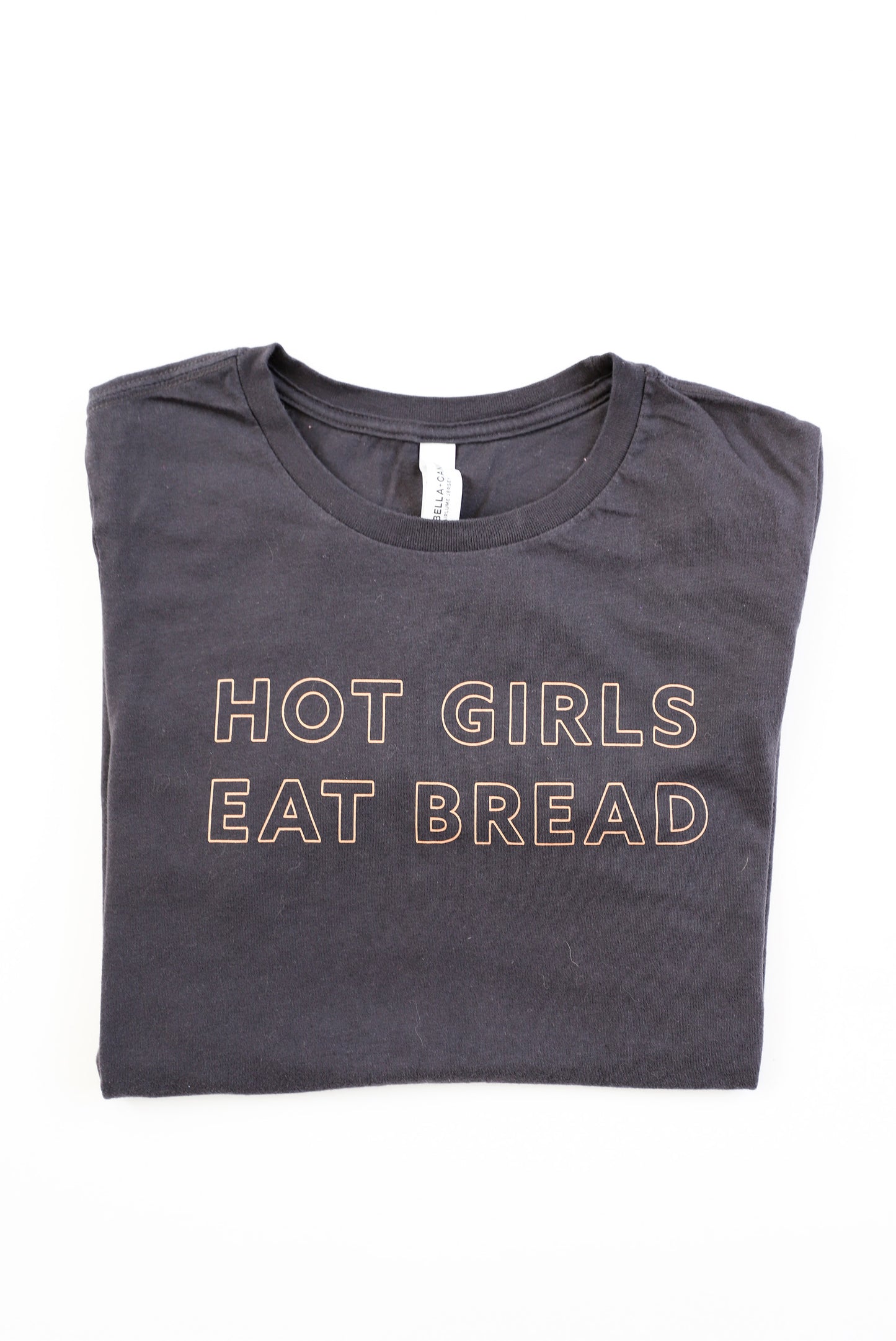 A folded dark grey t-shirt with the words Hot Girls Eat Bread and light pink letters
