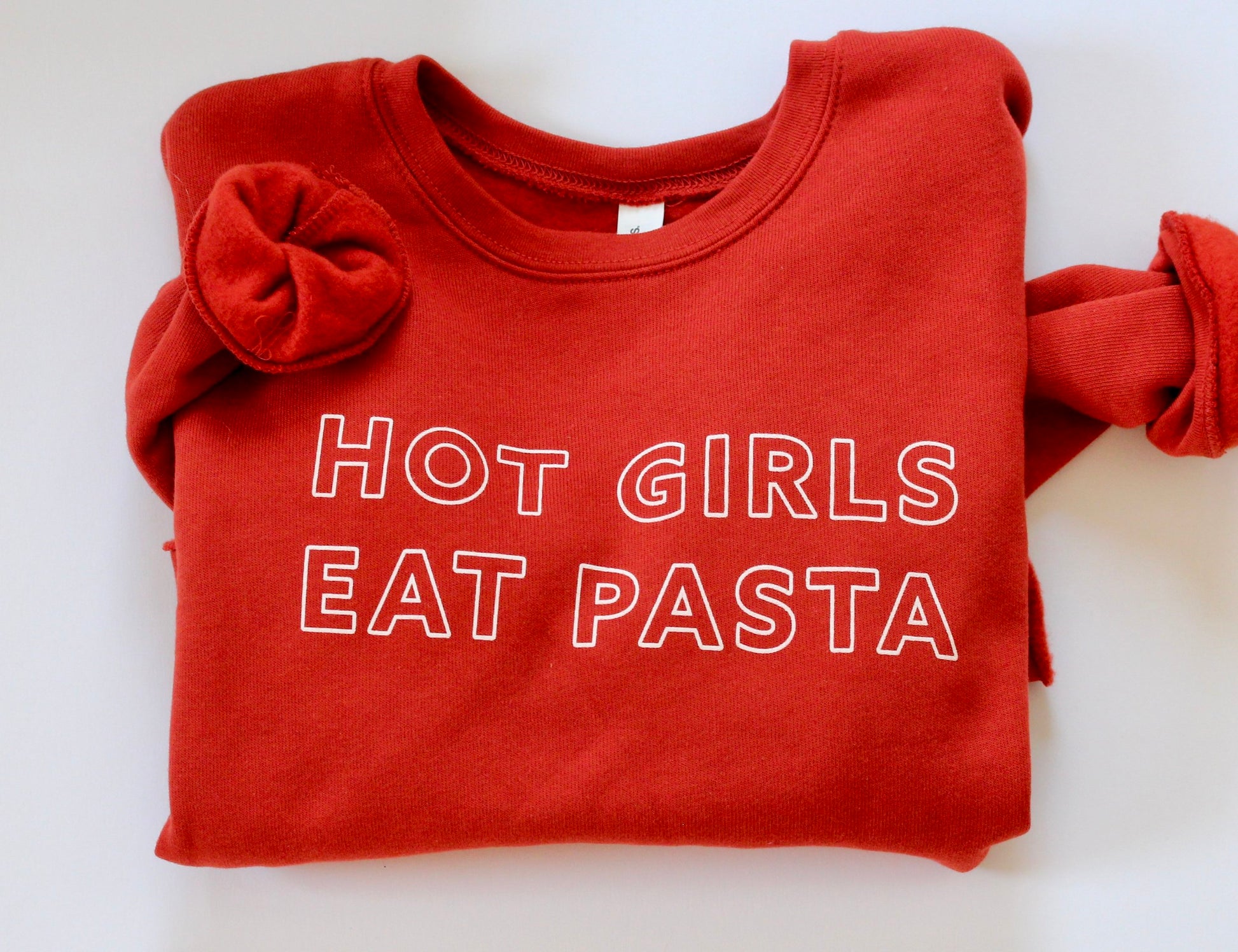 A folded cropped red crewneck with "Hot Girls Eat Pasta" written in white block letters