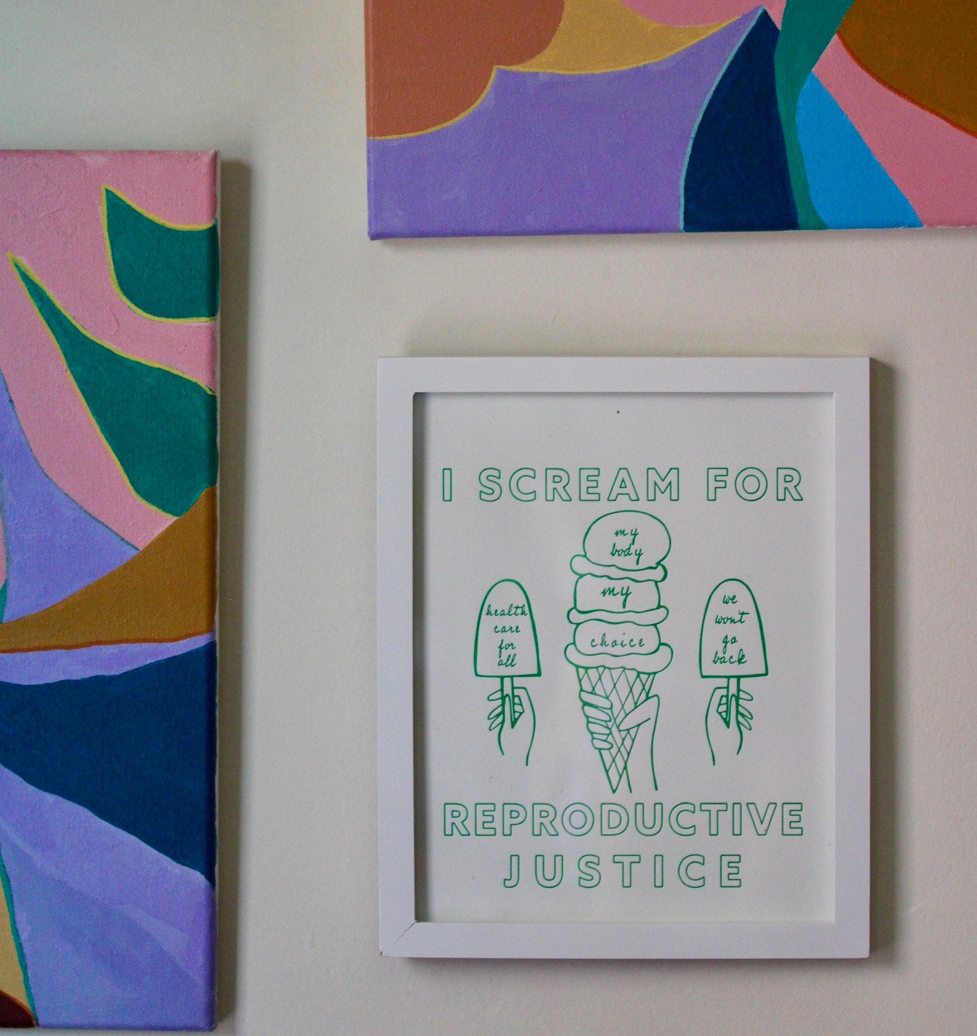 A framed print that reads "I Scream for Reproductive Justice" in mint green with ice cream illustrations on a wall
