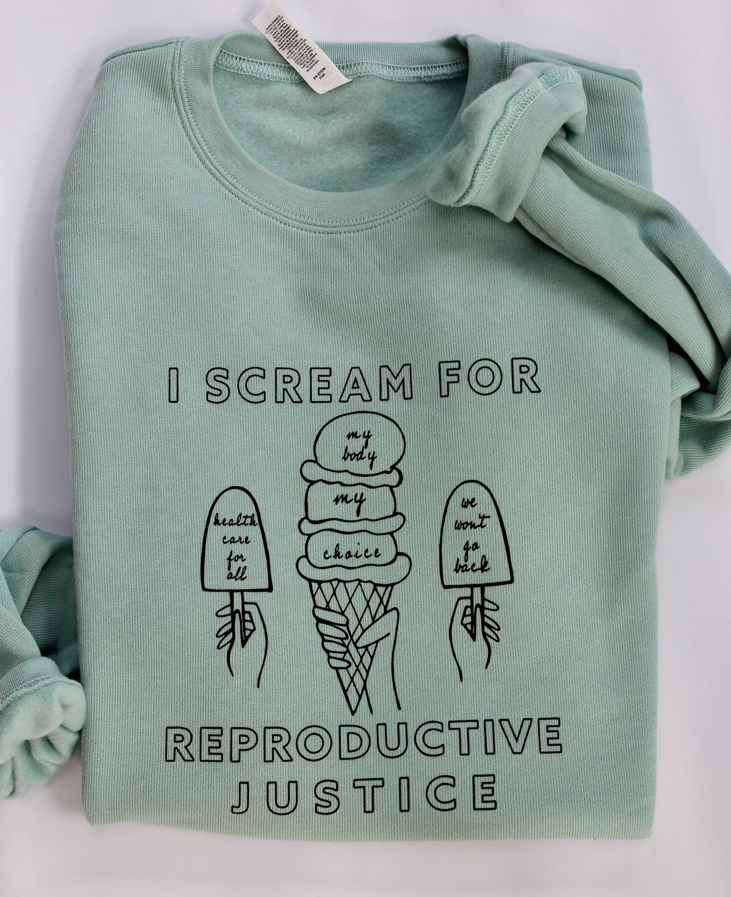 A folded dusty blue crewneck with "I Scream for Reproductive Justice" in black block letters and ice cream treat designs