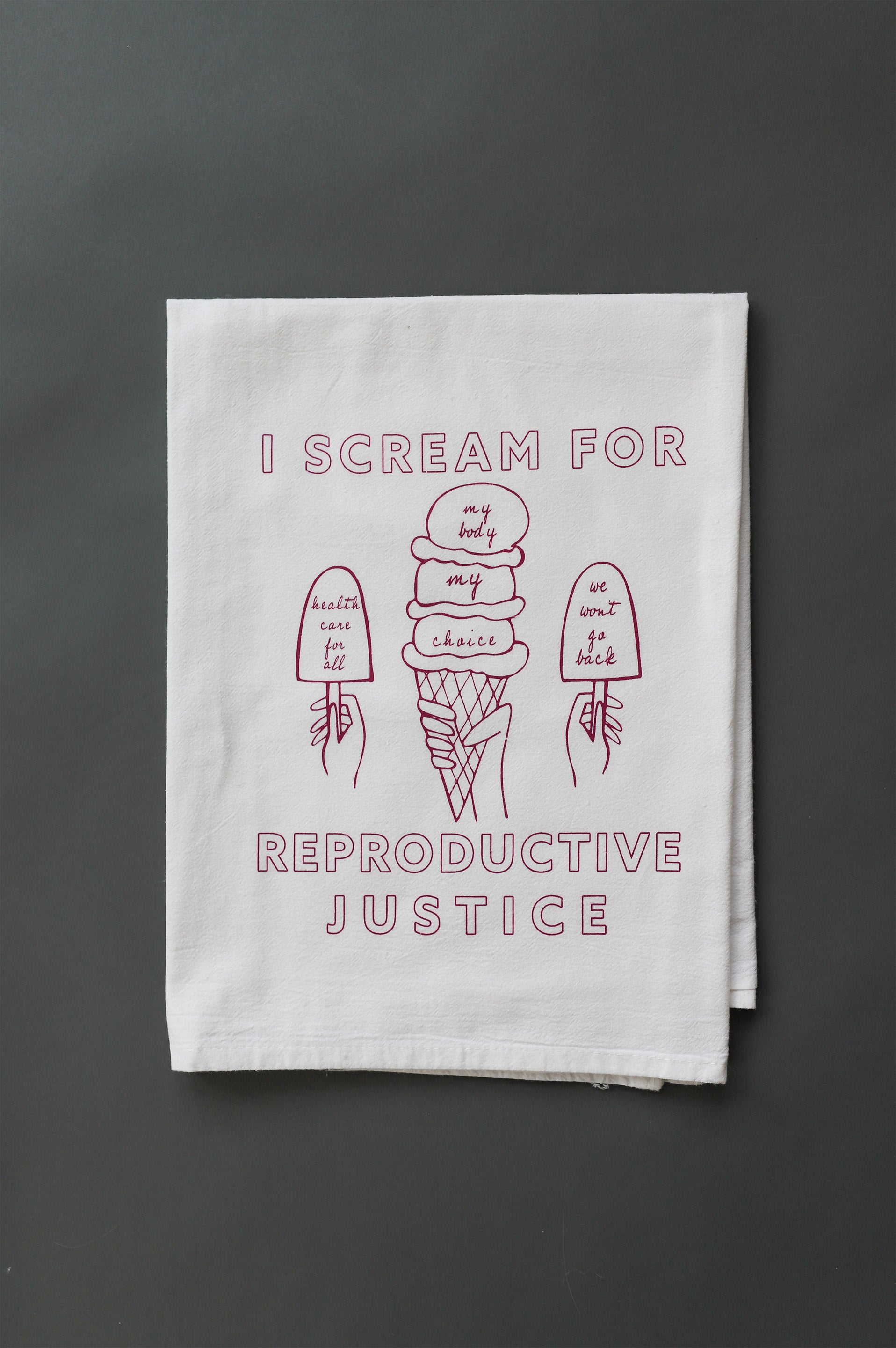 A white tea towel that reads I Scream for Reproductive Justice with ice cream designs in a raspberry color