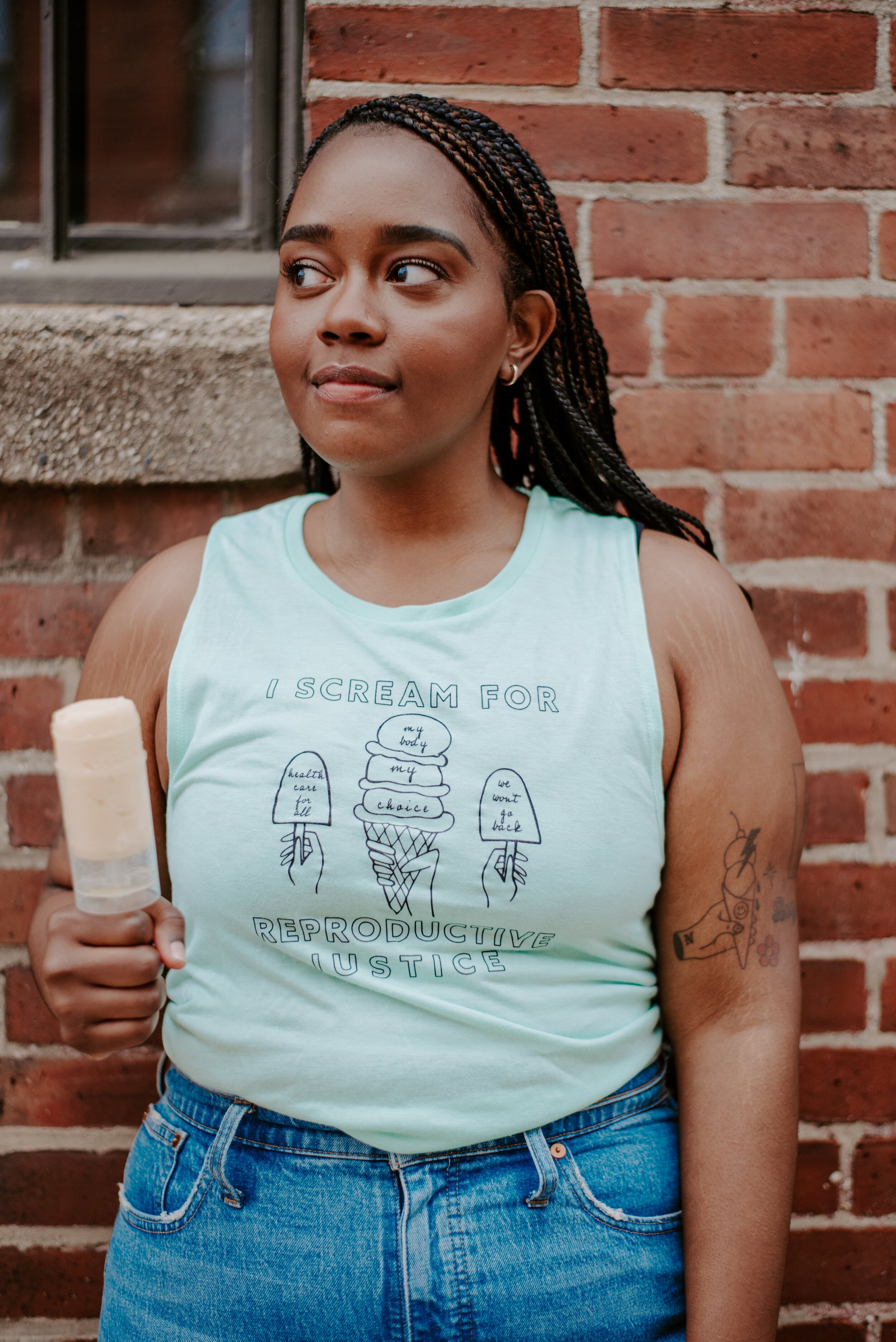 A woman wears a mint green tank that reads I Scream for Reproductive Justice and holds a frozen confection