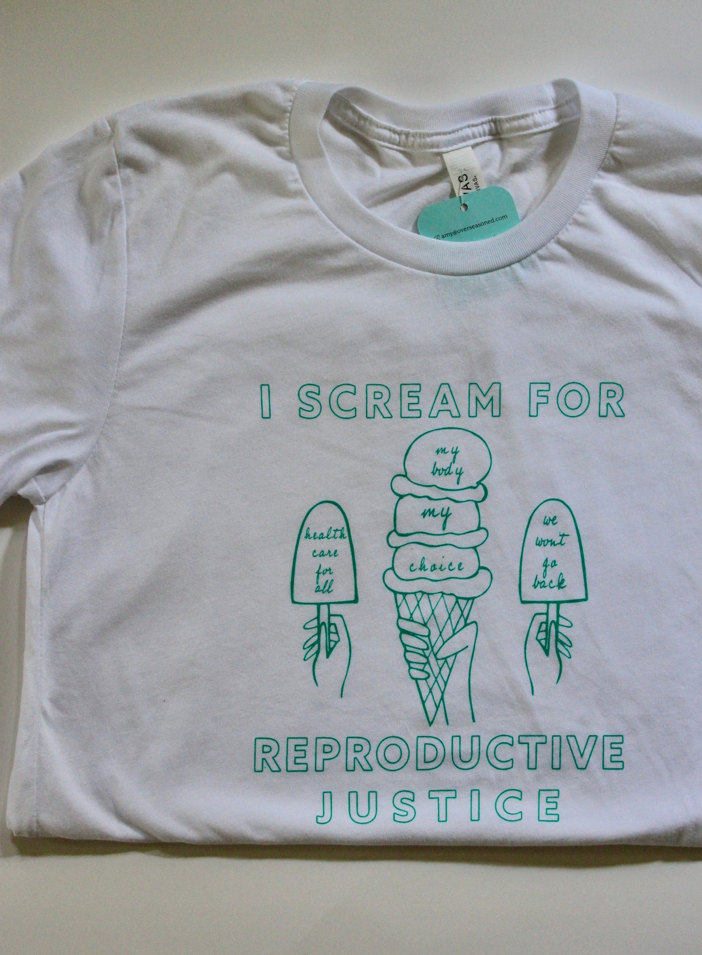 A white tee with the words I Scream for Reproductive Justice in mint green with ice cream illustrations
