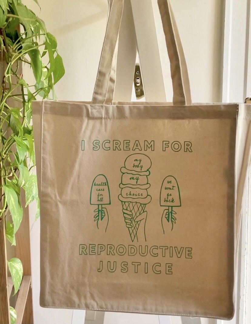 A canvas tote that reads "I Scream for Reproductive Justice" next to a house plant