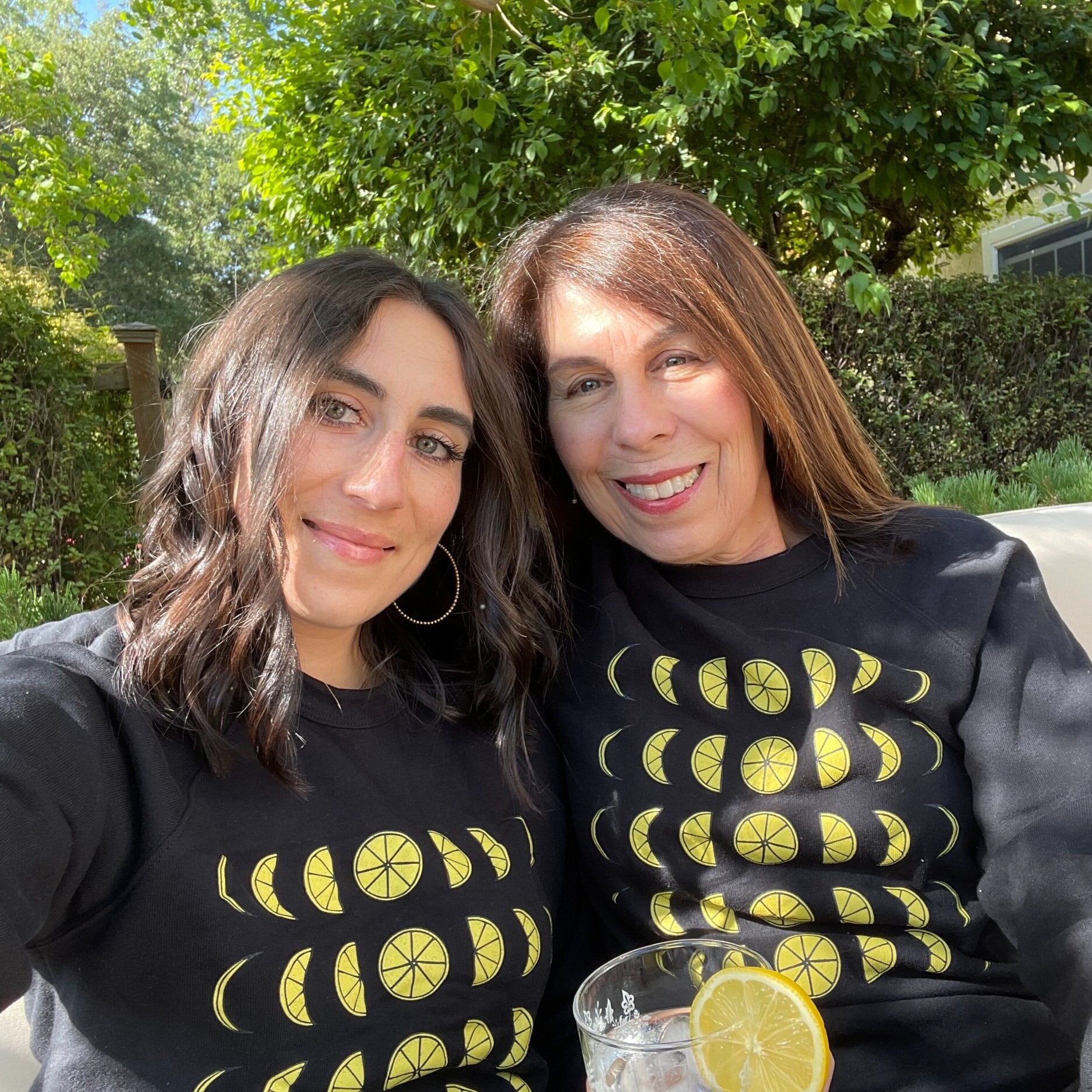 Two women wear matching black crewnecks with lemon moon phases
