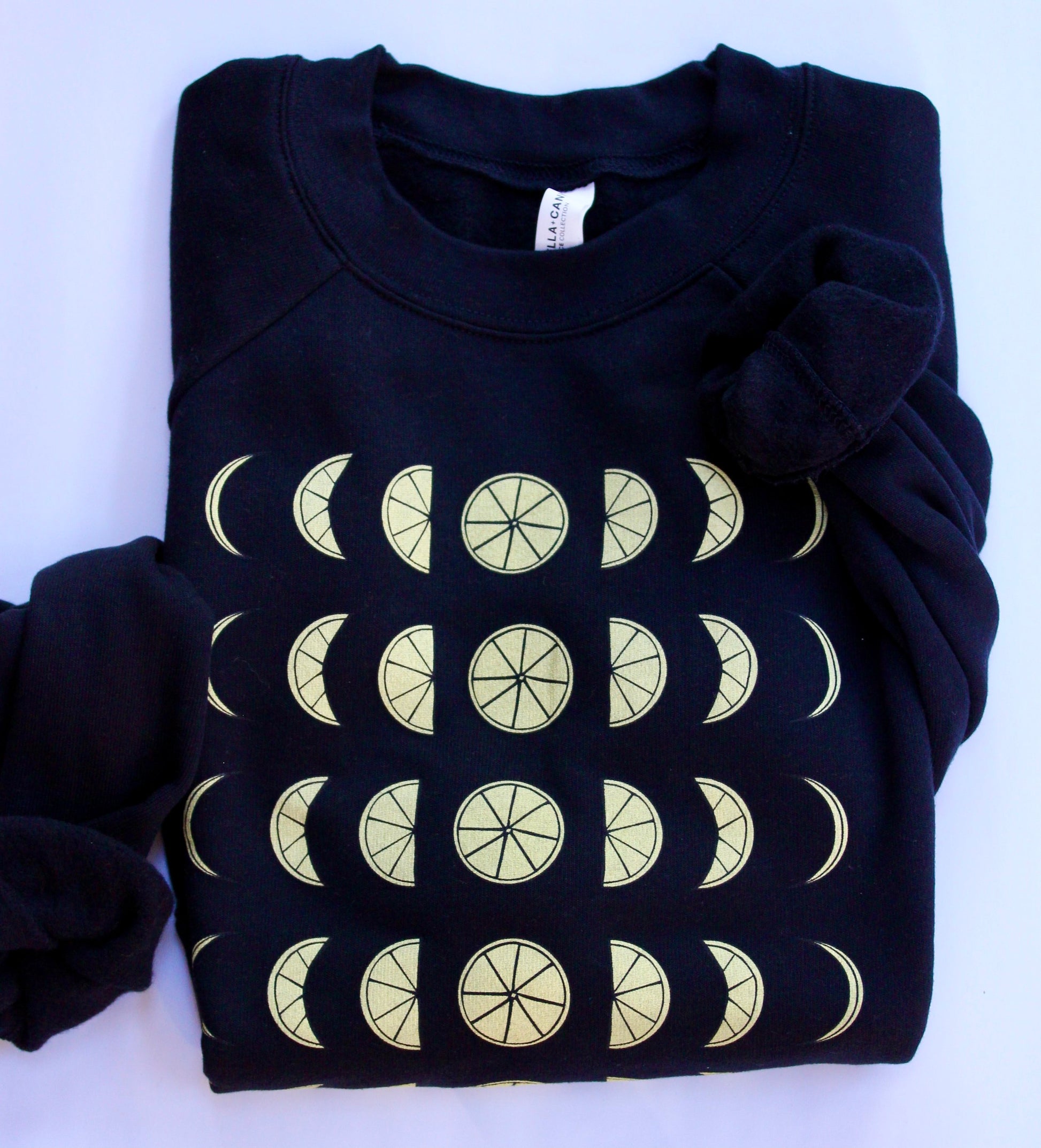 A folded cropped black sweatshirt with illustrated yellow lemons that resemble moon phases