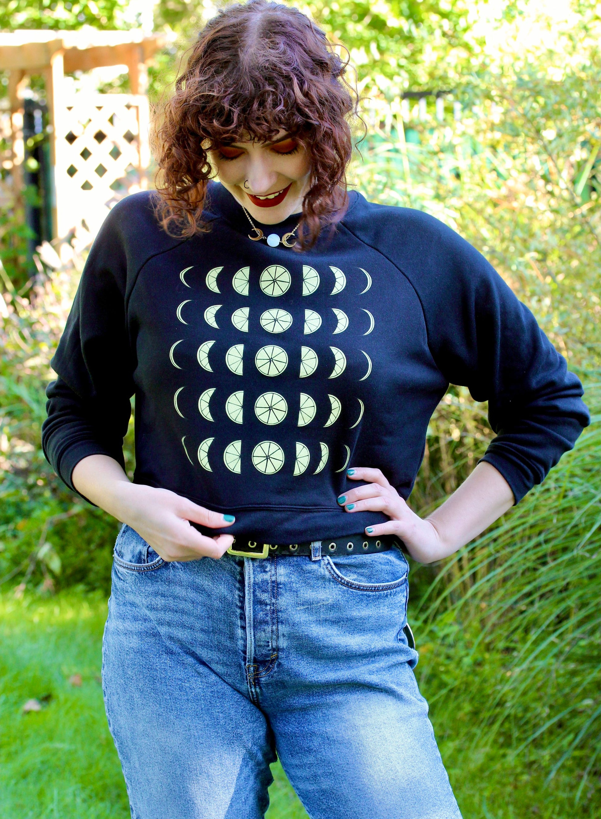 A woman wears a black cropped sweatshirt with lemon moon phase design with jeans