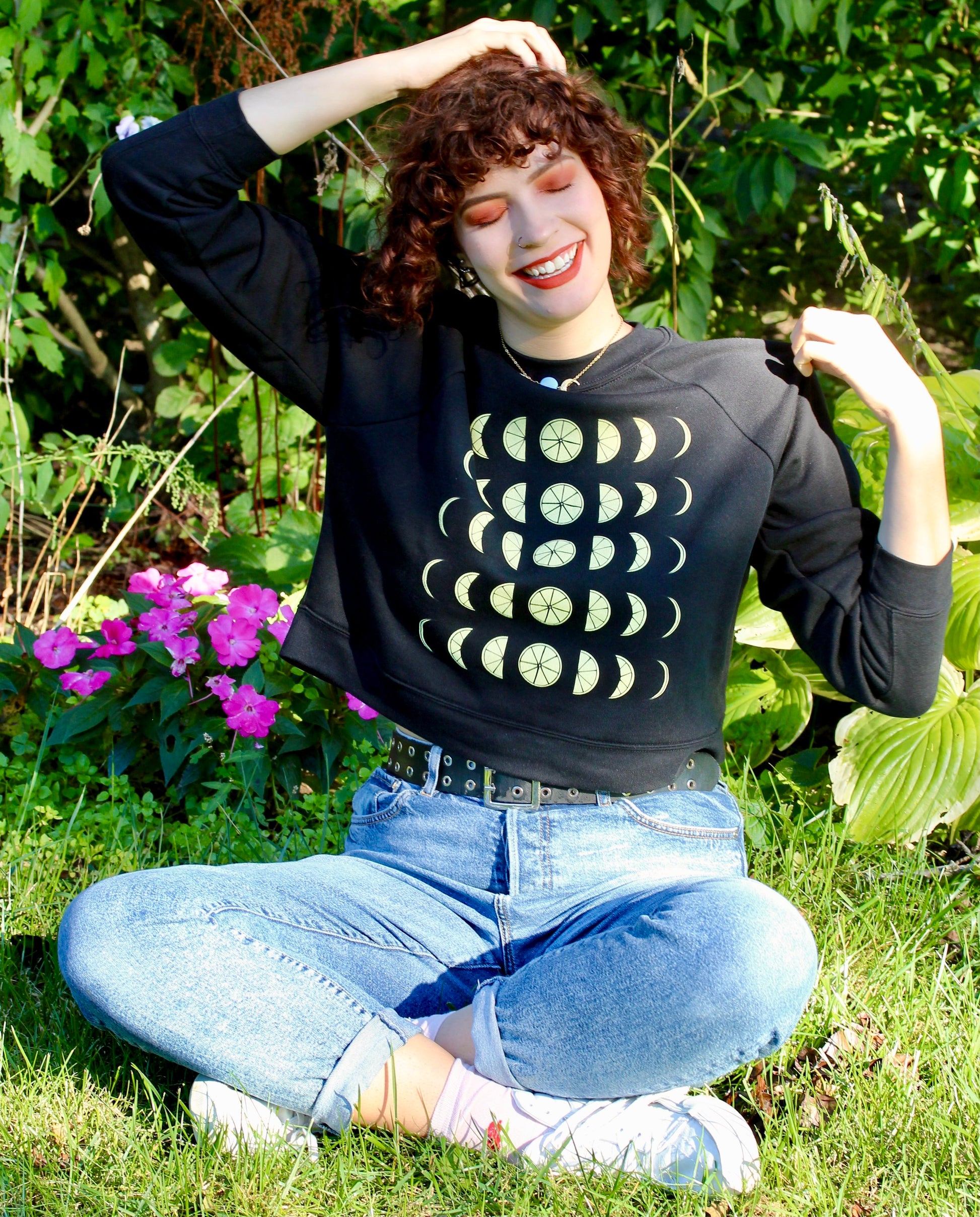 A woman in a black cropped sweatshirt with lemon design sits next to a garden