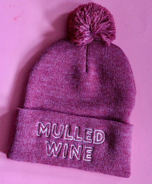 A berry pink beanie with pom pom and the words Mulled Wine in white embroidery