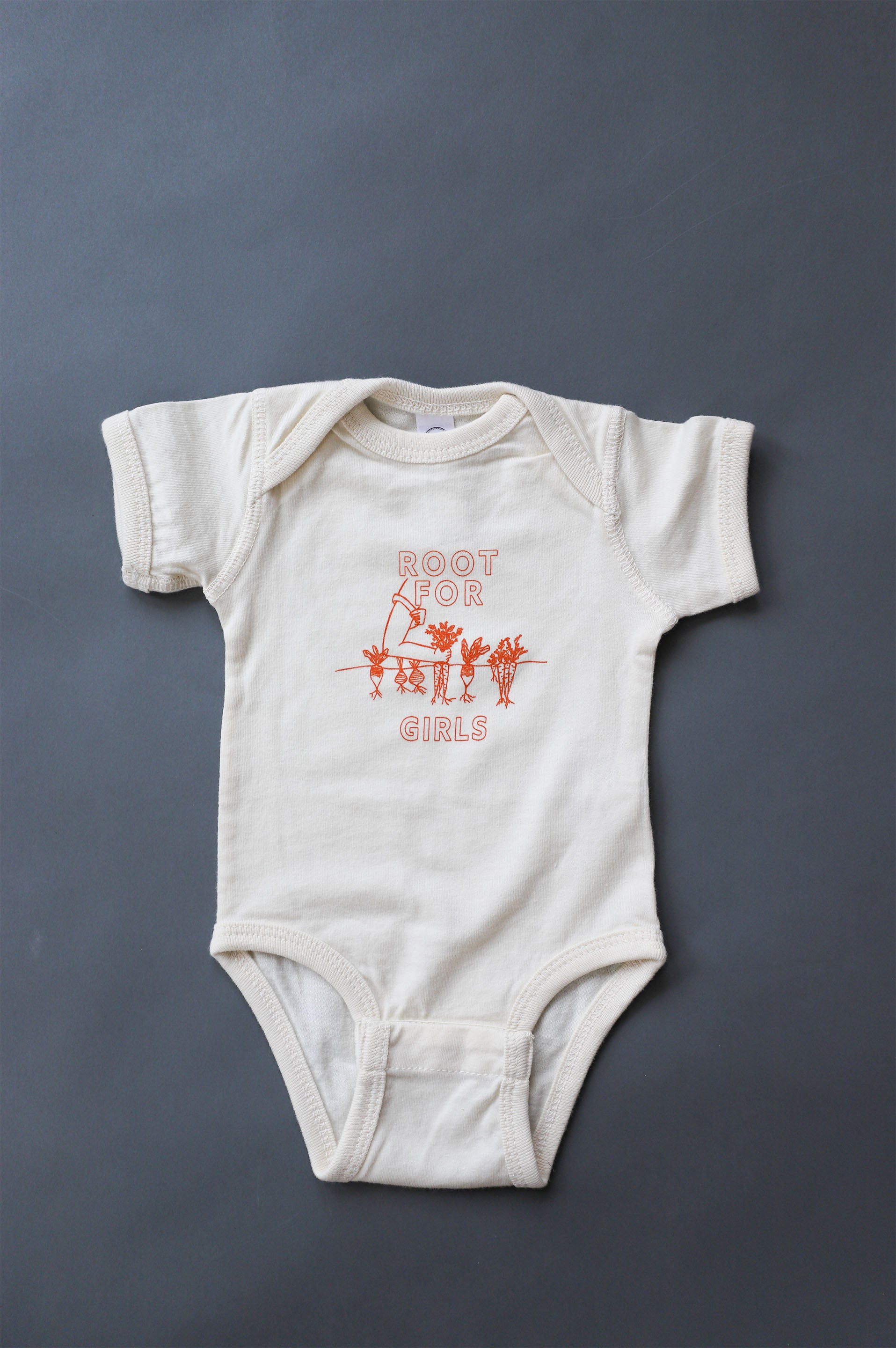 A natural color baby onesie with "Root for Girls" in dark orange and a gardening illustration 