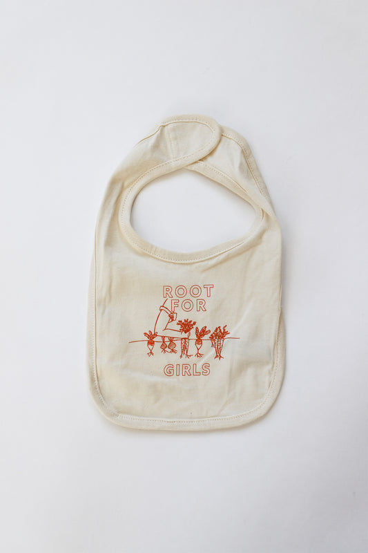 A beige baby bib with the words Root for Girls in orange block letters with garden illustration in carrot orange