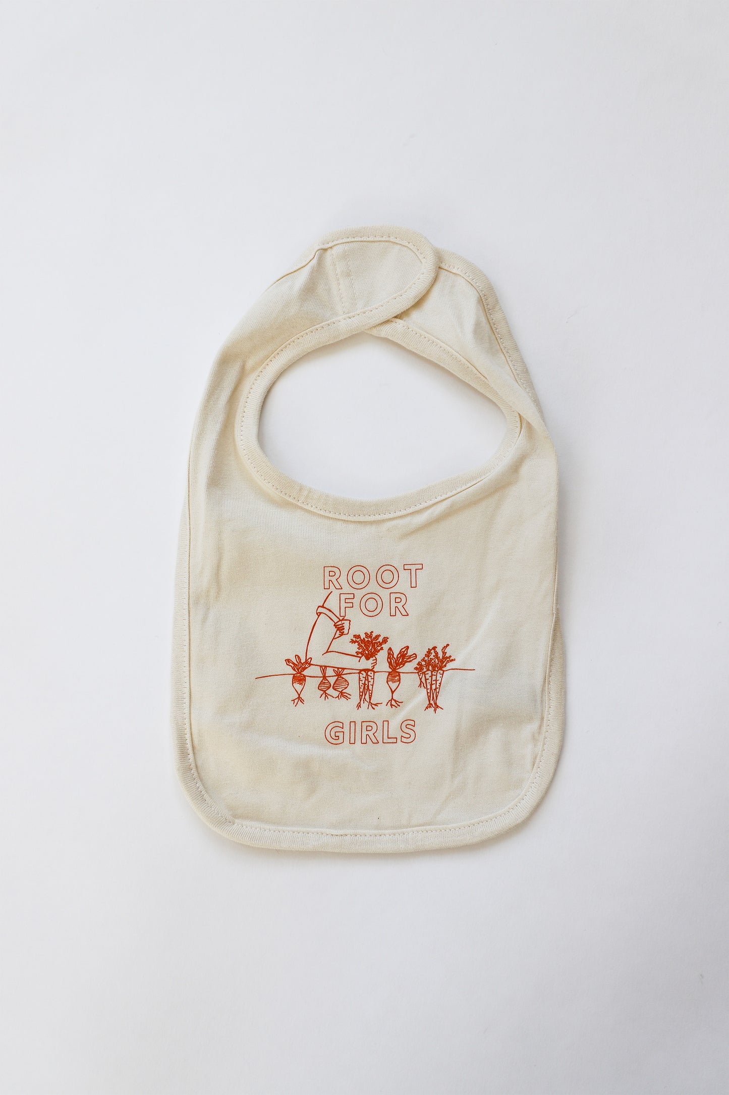 A beige baby bib with the words Root for Girls in orange block letters with garden illustration in carrot orange