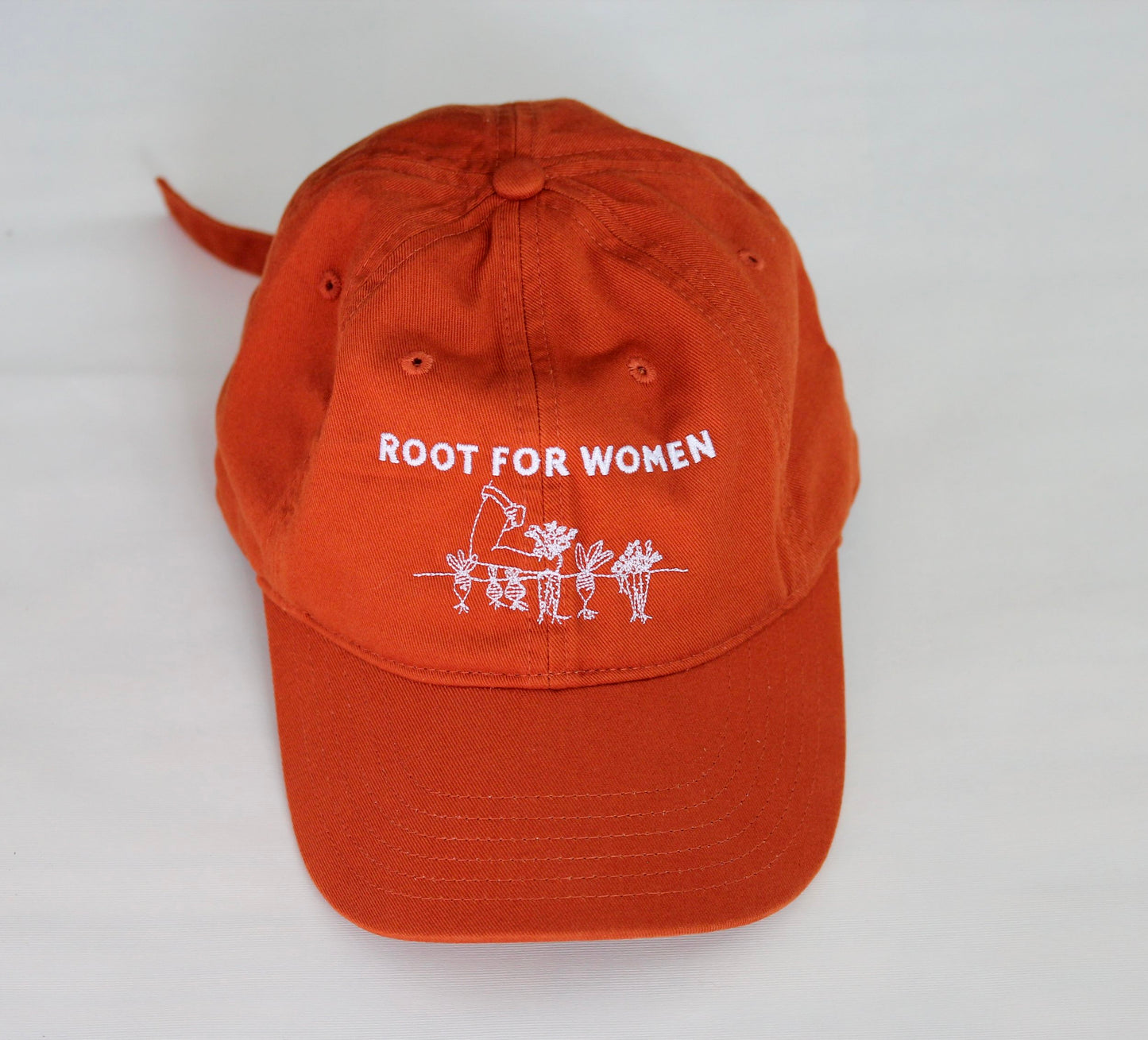 An orange baseball cap reads 'Root for women" in white embroidery 
