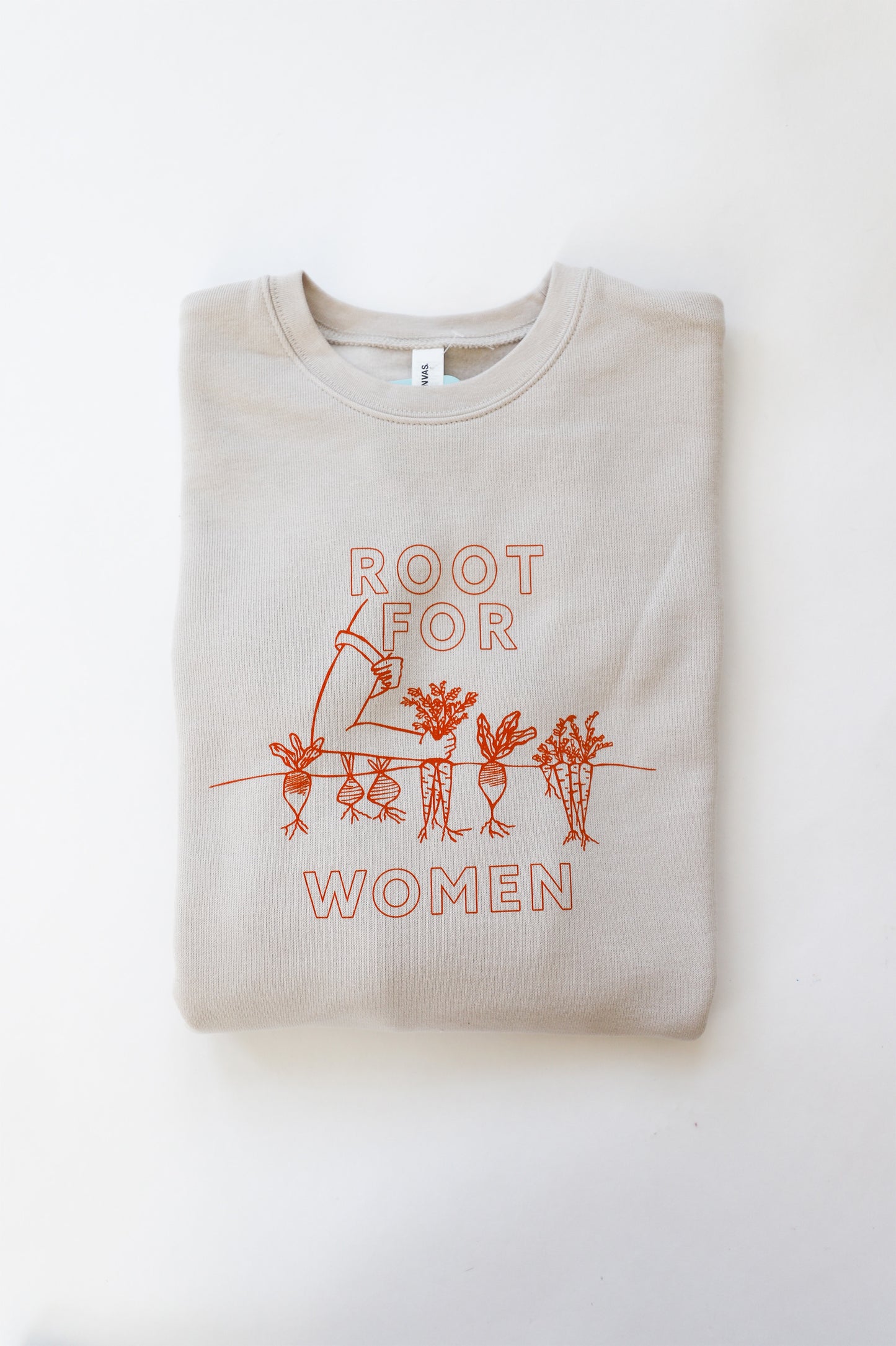 A folded natural color crewneck sweatshirt reads "Root For Women" in orange block letters