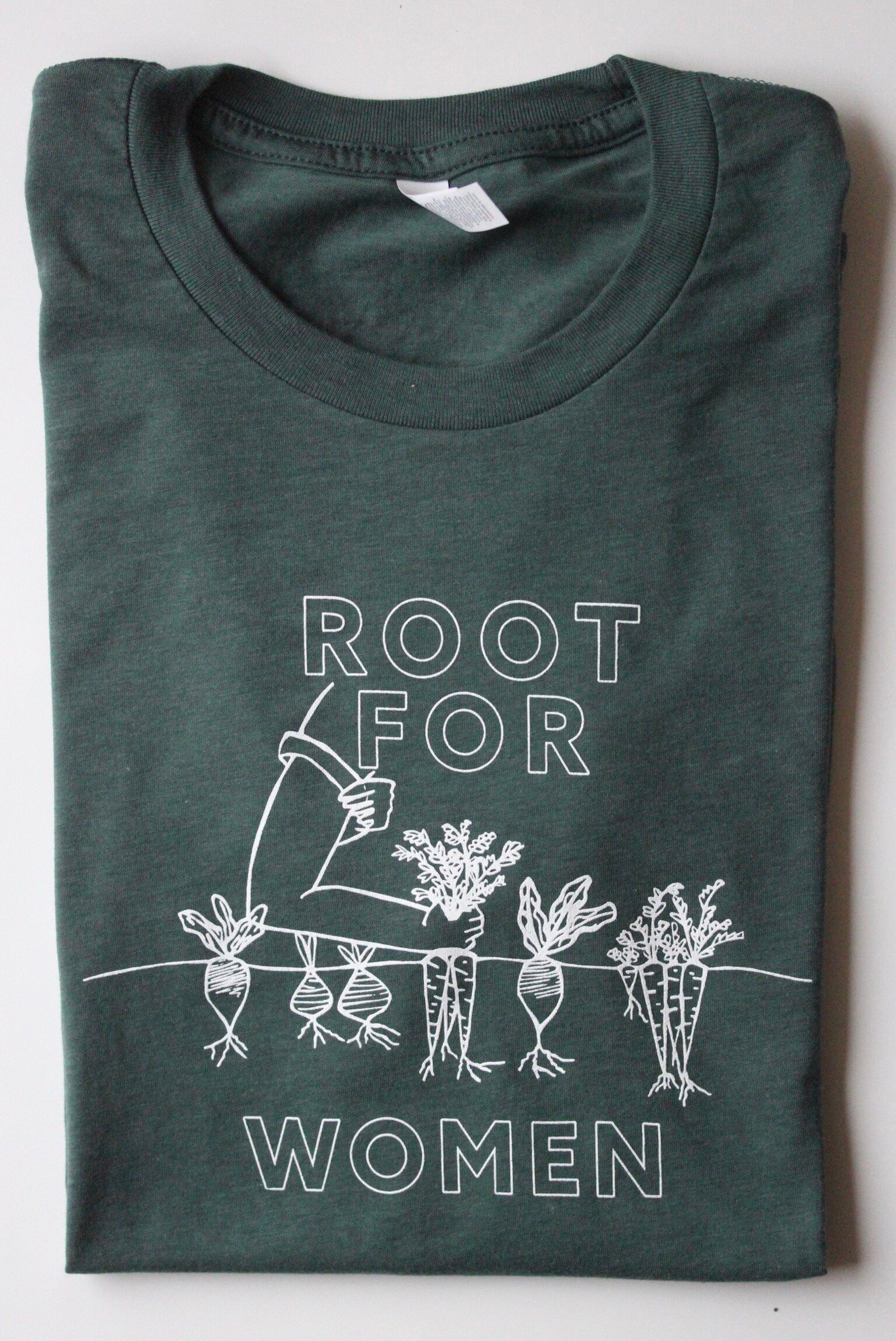 A folded green tee with white block letters reads "Root for Women"