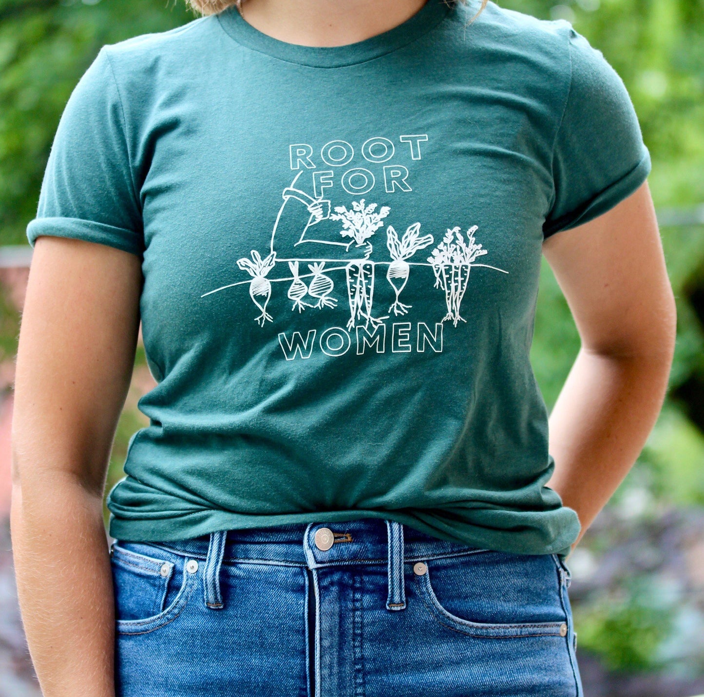 A woman wears a green t-shirt that reads "Root for Women" with jeans