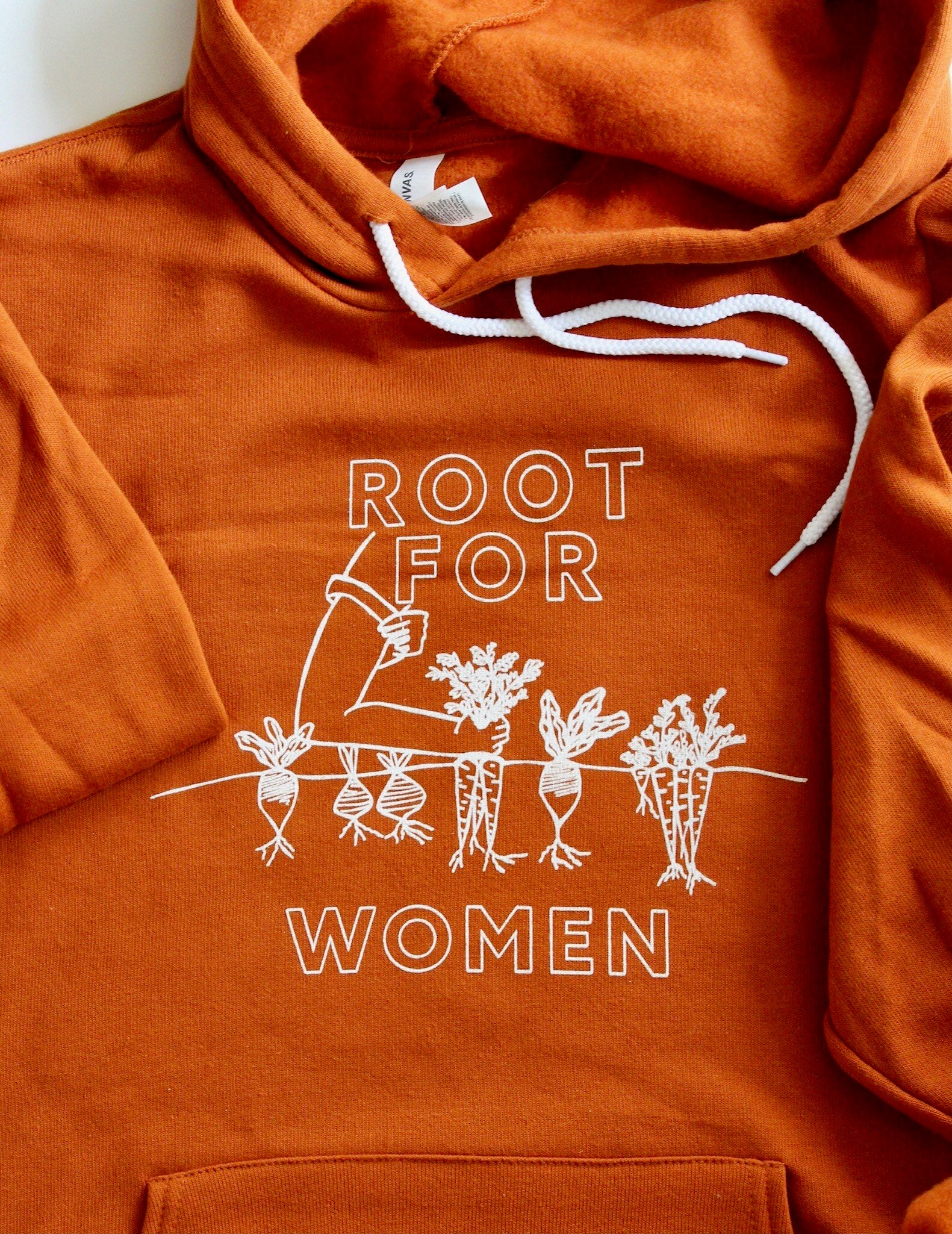 A close up of the "Root for Women" block letters and illustration on an orange hoodie