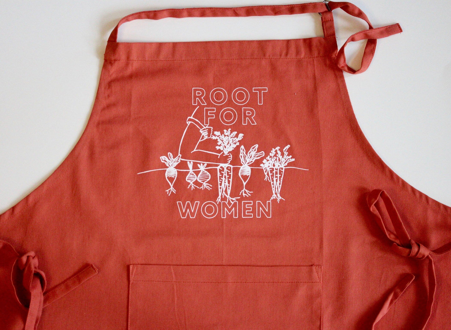 A carrot orange apron that reads "Root for Women" in white block letters with garden illustration