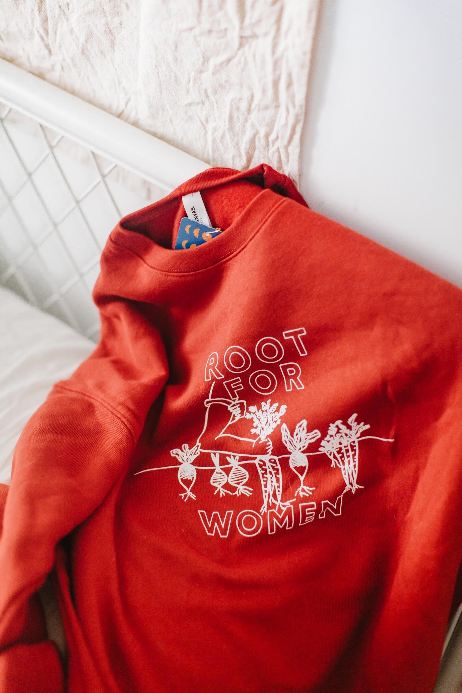 A red "Root for Women" sweatshirt draped on a bed frame