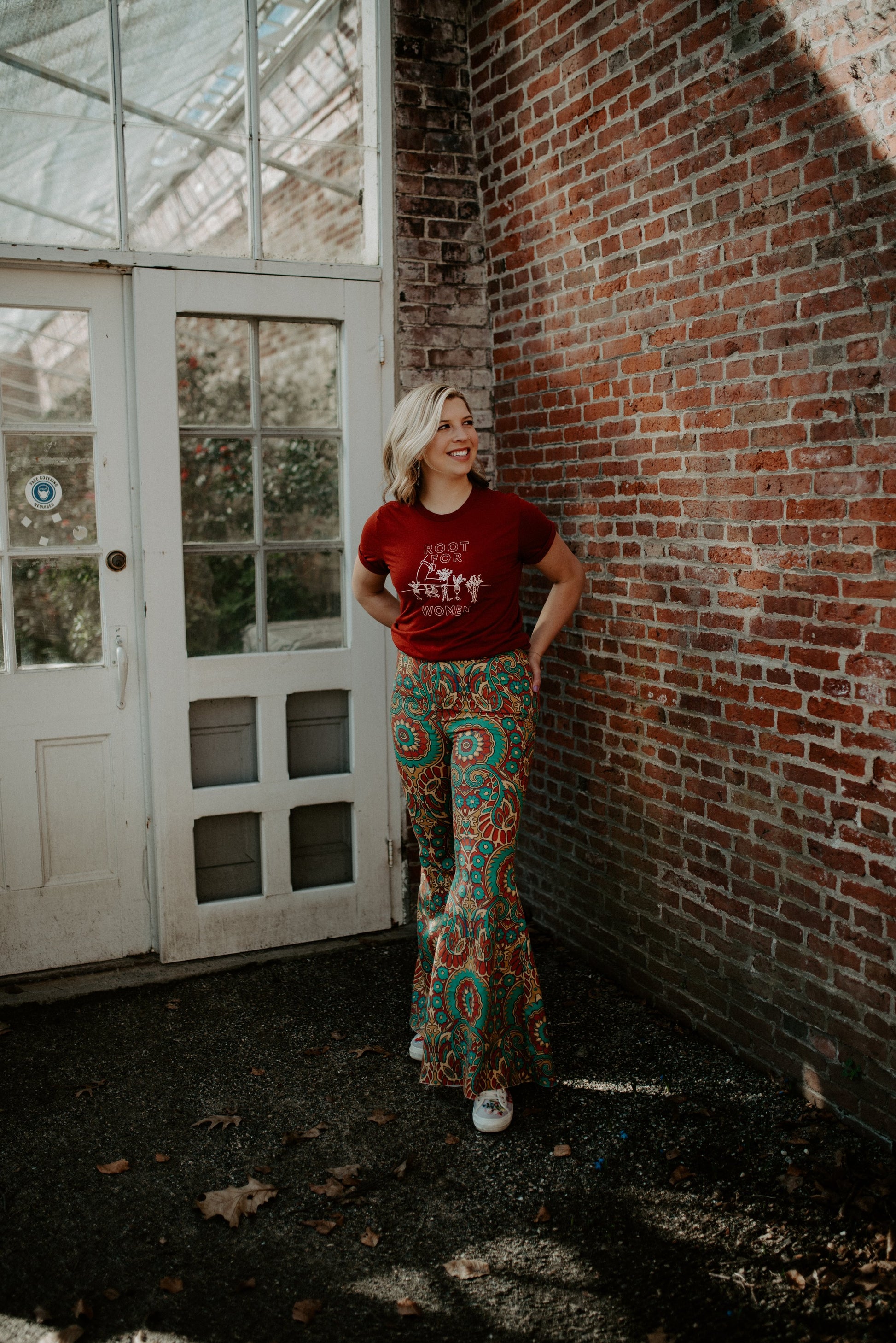 A woman wears a red Root for Women t-shirt with colorful paisley pants