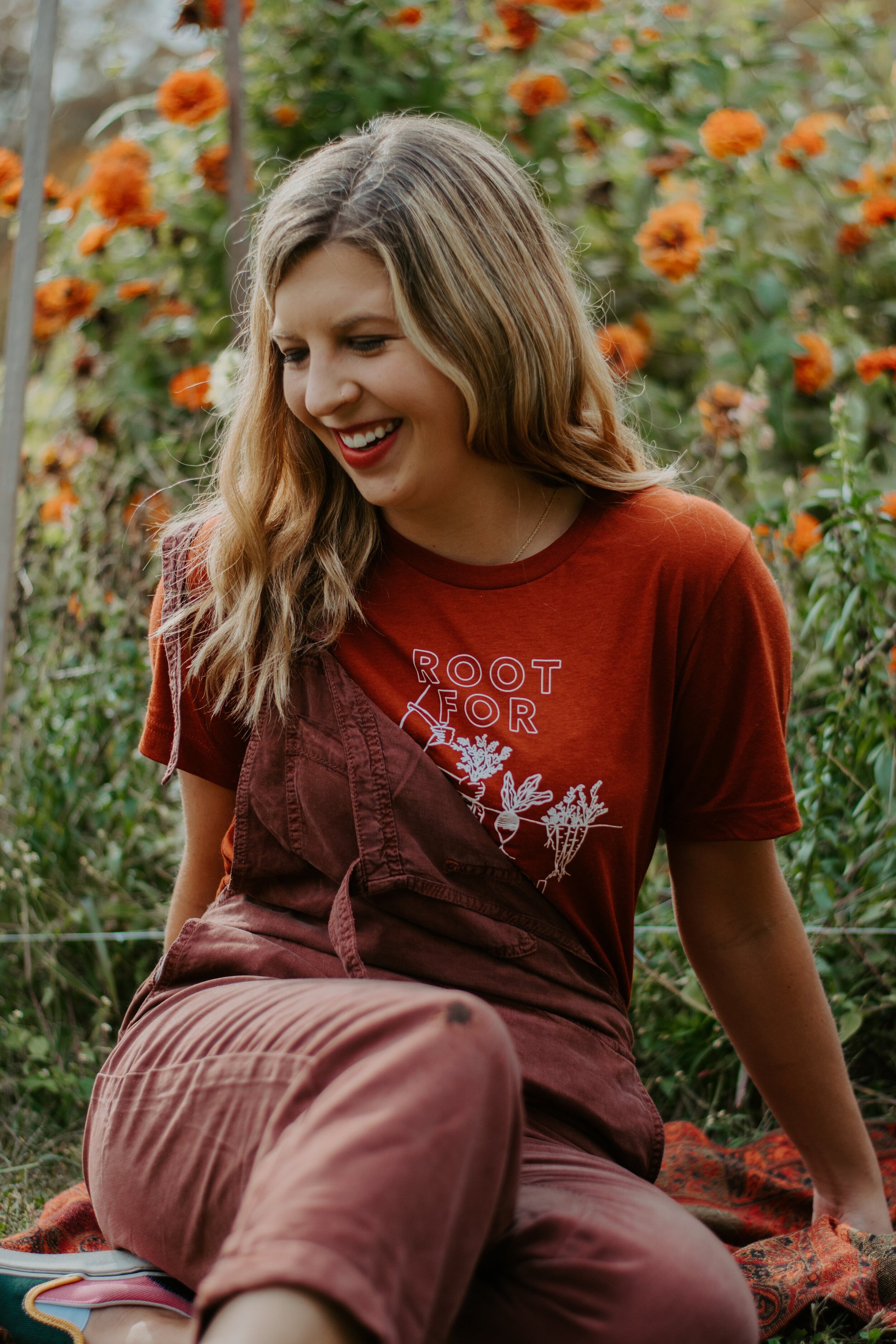 A woman wears a red t-shirt that reads "Root for Women" with brown overalls