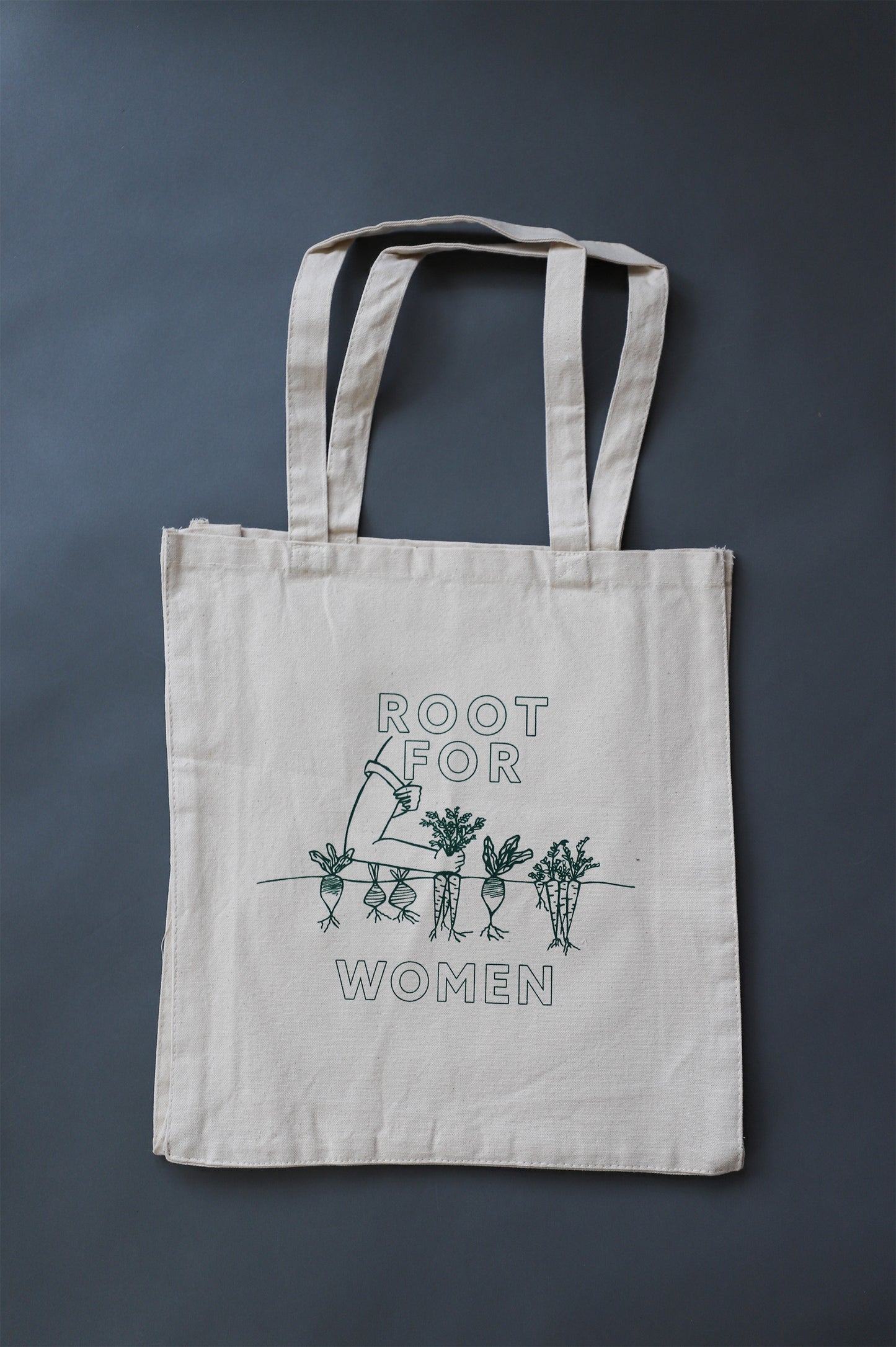 A canvas tote with the words "Root for Women" in green block letters and a garden illustration 