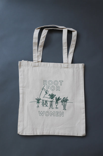A canvas tote with the words "Root for Women" in green block letters and a garden illustration 