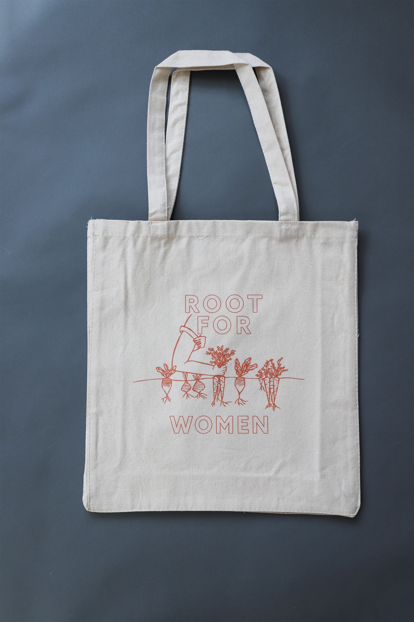 A canvas tote with red block letters reads "Root for Women" with a garden illustration 