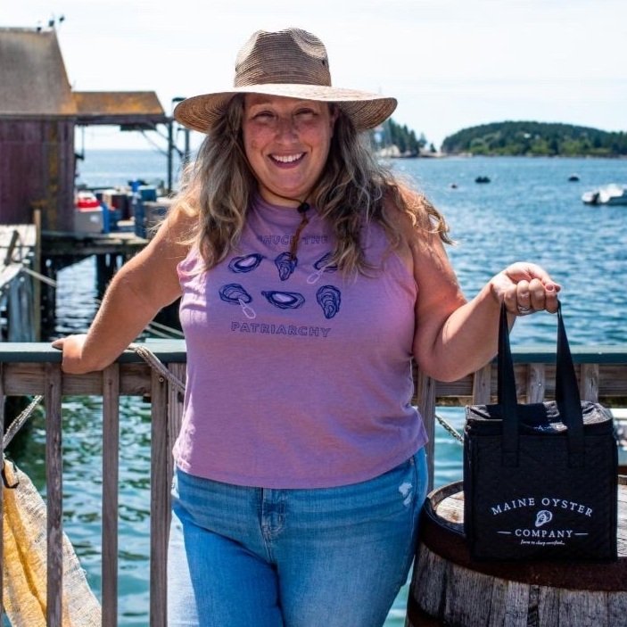 A woman wears a cropped tank that reads "Shuck the Patriarchy" on a dock