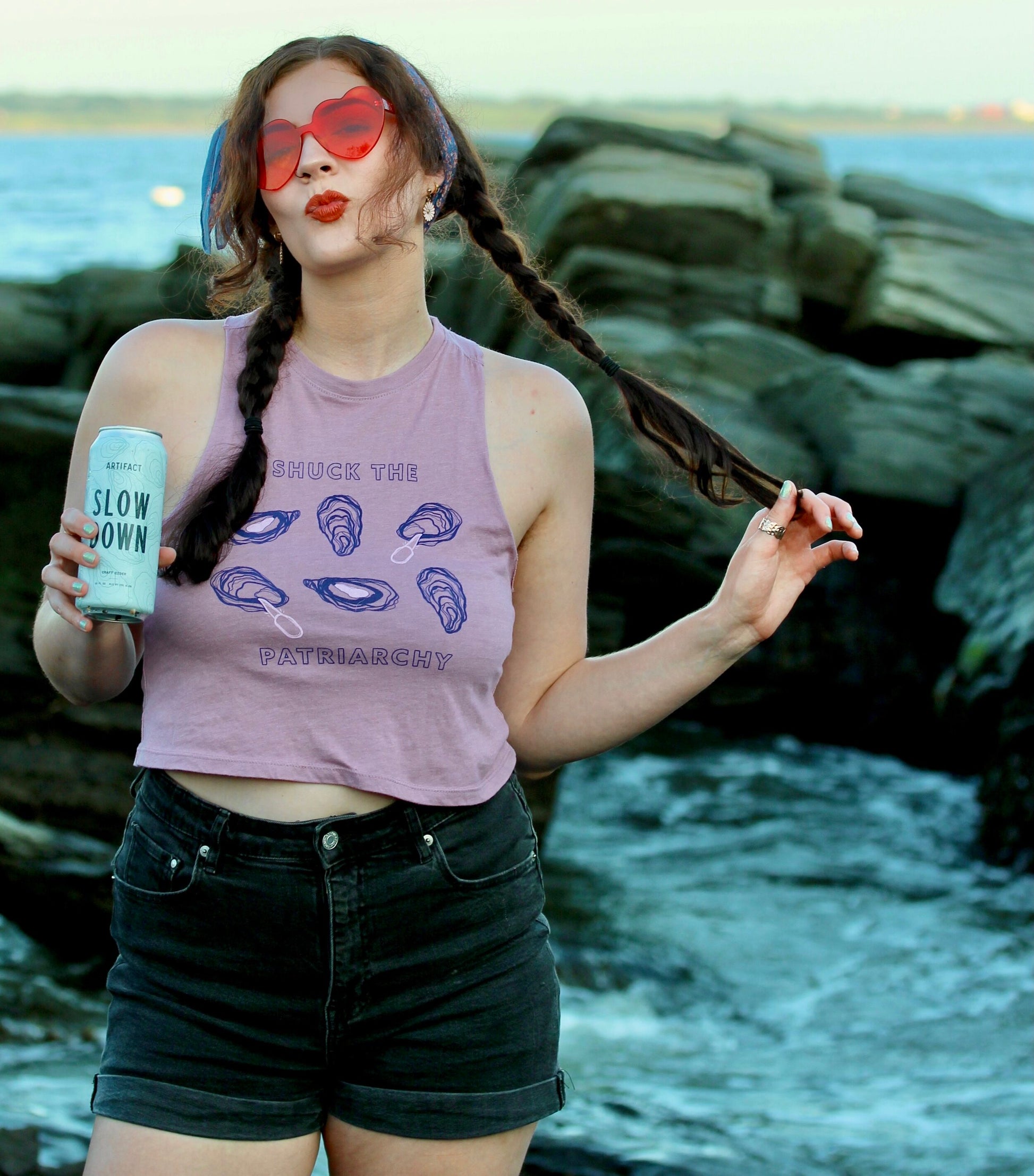 A woman wears a "Shuck the Patriarchy" crop tank with dark denim shorts