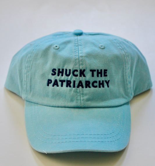 A light blue hat reads "Shuck the Patriarchy" in dark blue embroidery