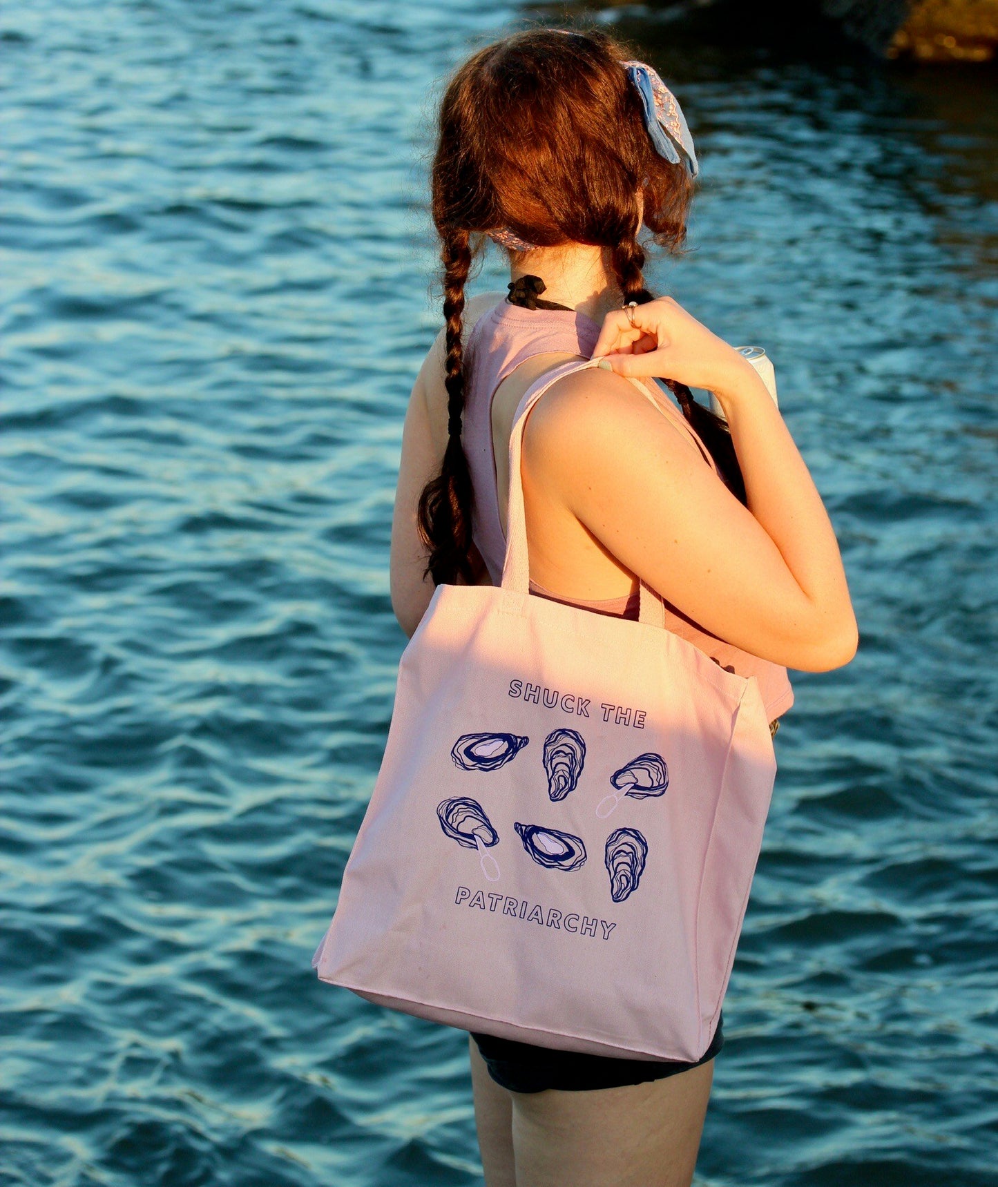 A woman wears a pink canvas tote that reads "Shuck the Patriarchy" at the beach