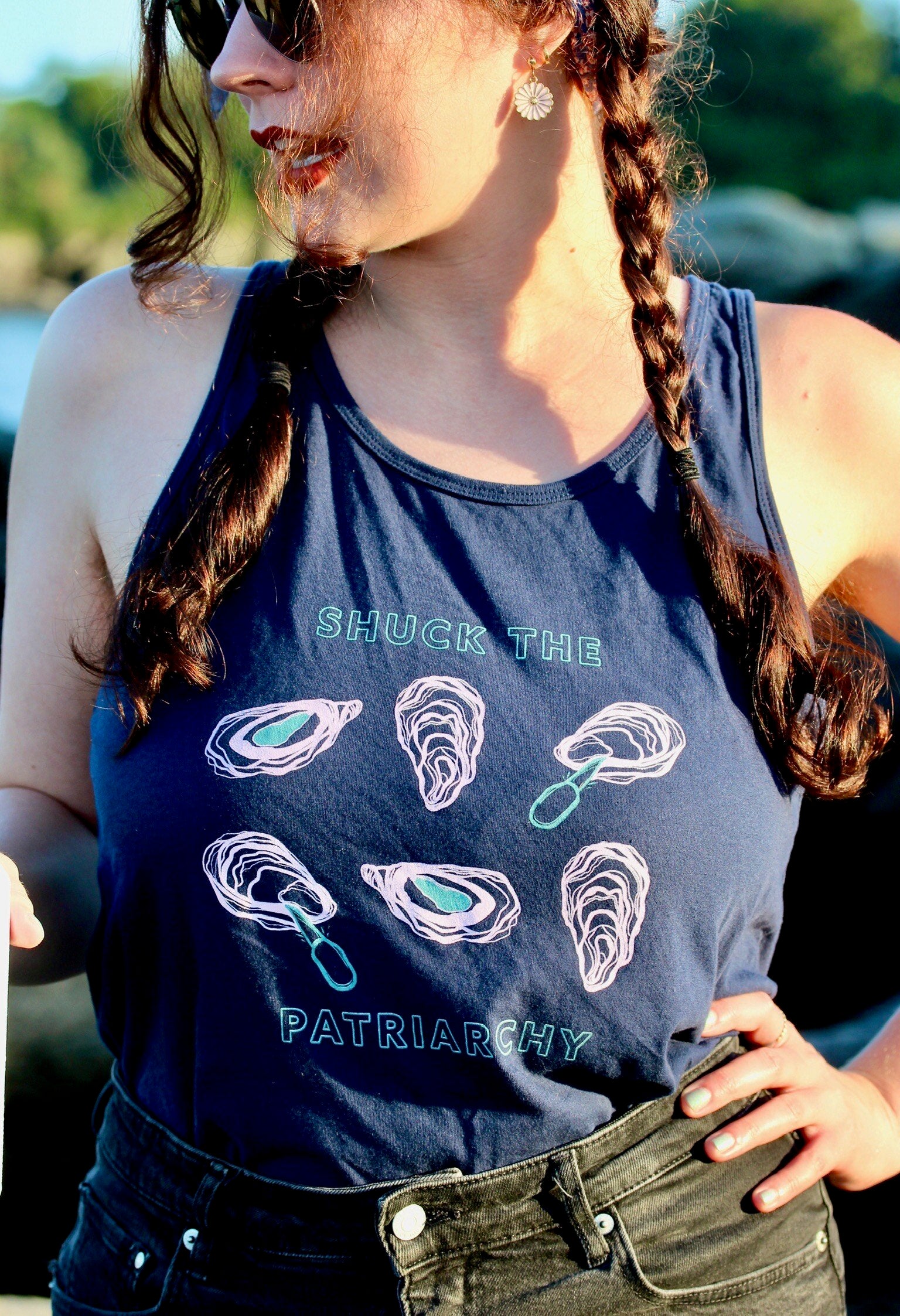A woman wears a navy blue tank that reads "Shuck the Patriarchy" with oyster illustrations 