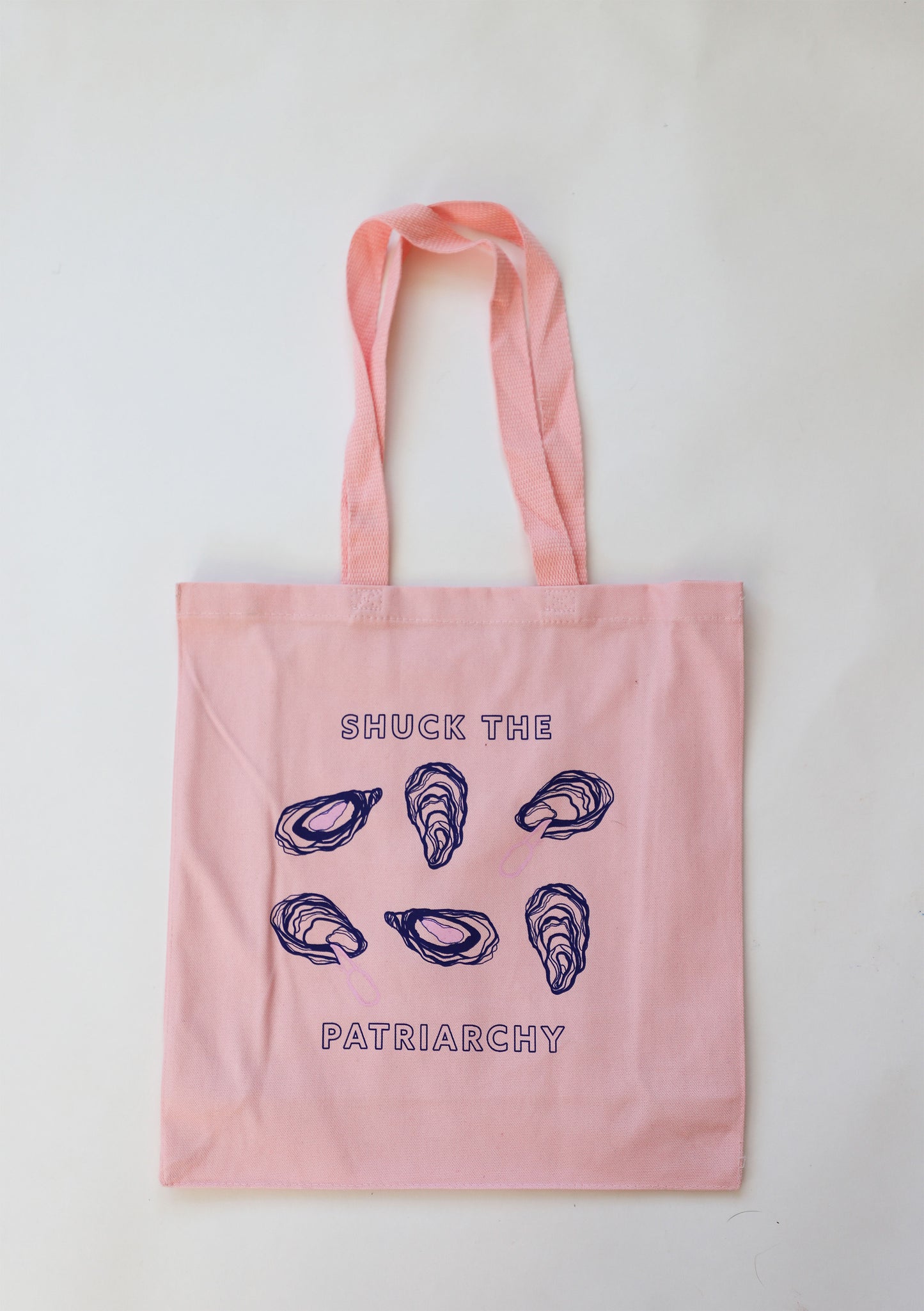 A pink canvas tote that reads "Shuck the Patriarchy" with oyster designs