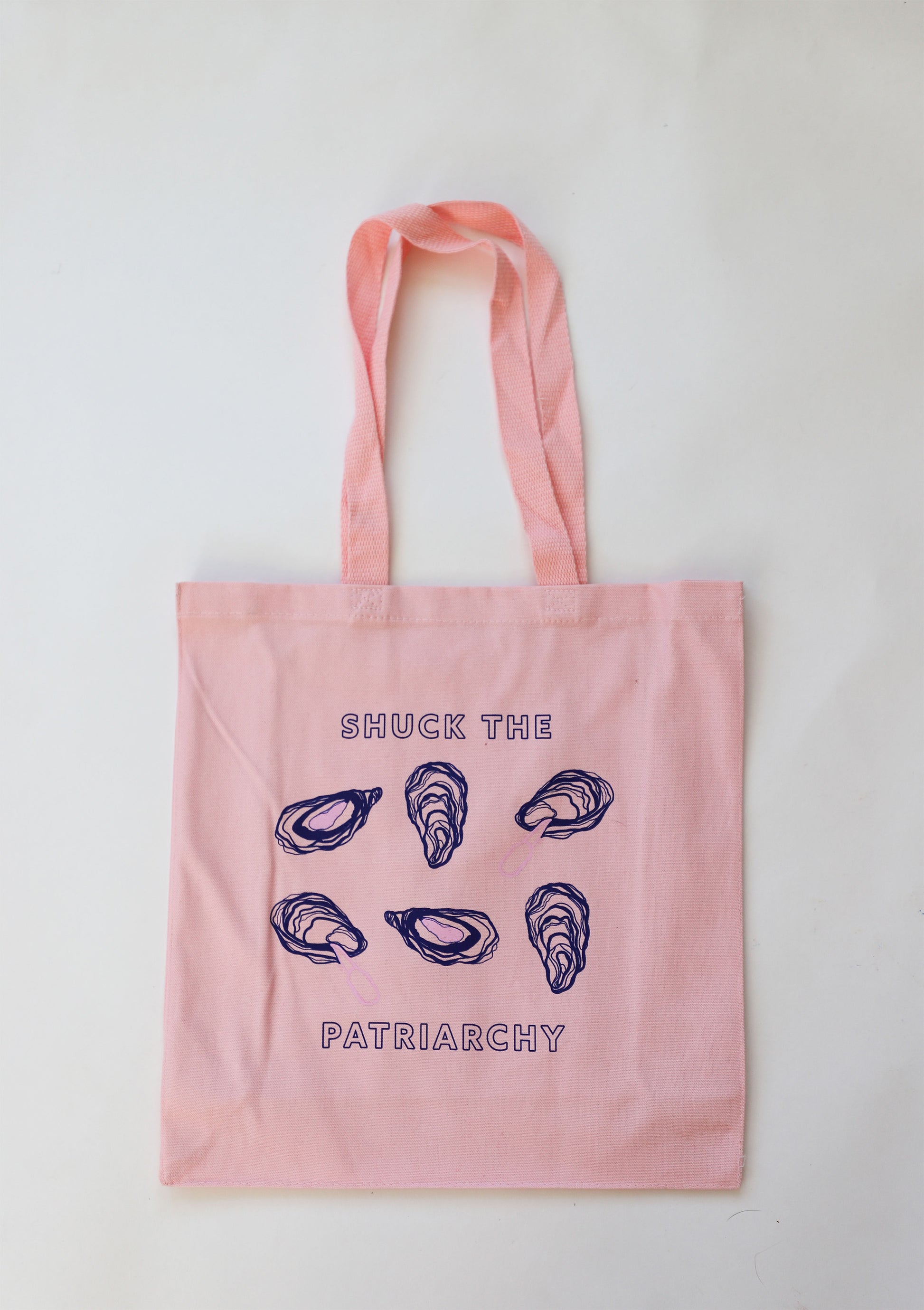 A pink canvas tote that reads "Shuck the Patriarchy" with oyster designs